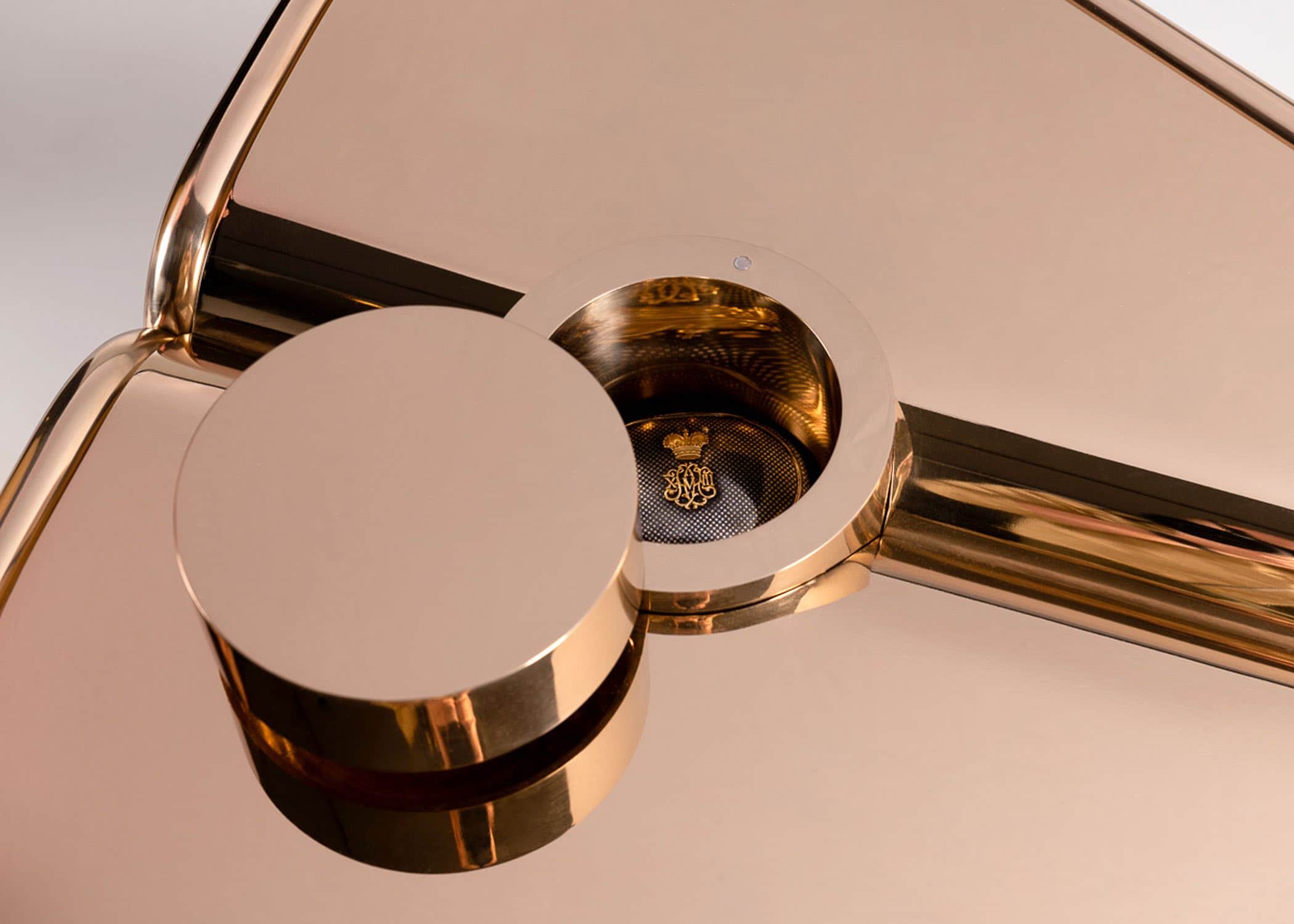 This image shows a close-up detail plan view of Second Empress Coffee Table designed by Carol Egan. Machined and polished silicon bronze cocktail coffee table with Upper and lower planes at opposing angles mirrored and intersected by a cylindrical form with swivel lid to reveal a concealed storage space.  The peripheral form of the coffee table is trimmed by a bisecting cylindrical edging.  The table is cantilevered from the upright cylindrical form to hover above the ground.  Dimensions of table are 26"w x 25"d x 16”h.