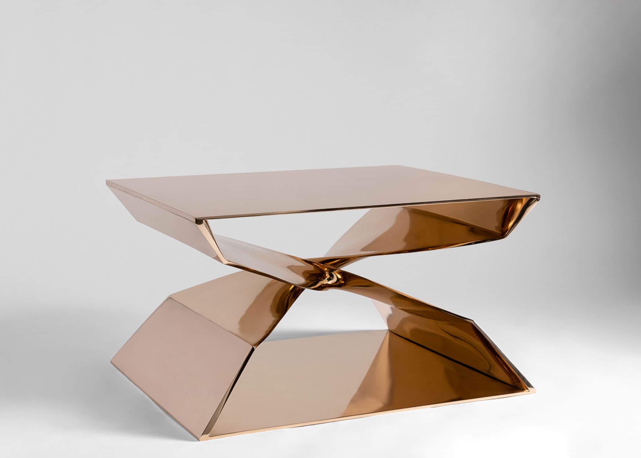 Set against a grey background this image shows the large-scale X shaped coffee table designed by carol Egan.  CE24 Cast Silicon bronze X shaped coffee table with mirror polished finish.  30" w x 24" d x 18"h.  The view shows the table placed diagonally.