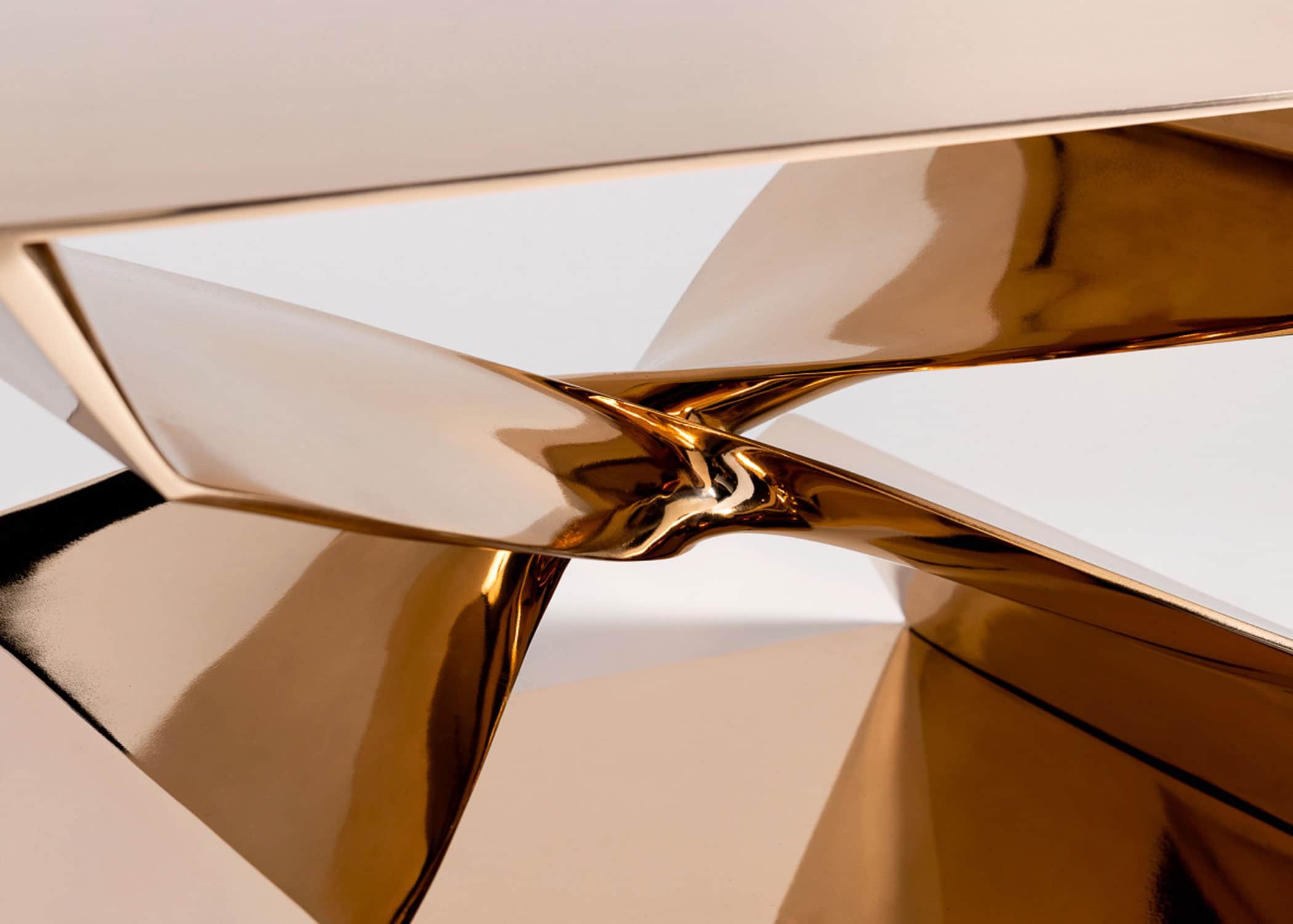 This image shows a close-up detail of the center intersection of the cast X shaped Coffee Table designed by Carol Egan.  The CE24 Cast Silicon bronze X shaped coffee table has a mirror polished finish.   The dimensions of the table are 30"w x 24"d x 18"h. This close-up detailed view illustrates the reflections and the casting details of the center section of the base of the table.
