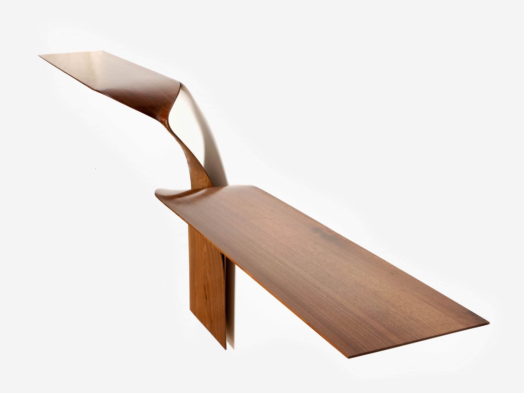 The image shows a 45-degree angle of the CE02 American Walnut two arm asymmetrical wall console designed by Carol Egan.  The piece has a hand Carved Finish and is a sculptural form that is cantilevered from the wall.  Shown here is a view of the Front Elevation. Dimensions 29"h X 96"w X 12"d (74 X 244 X 30cm).