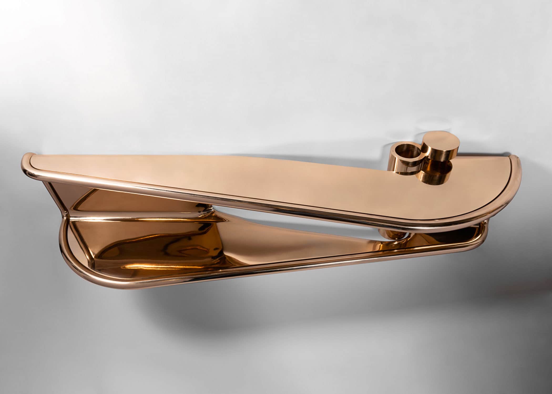 Designed by Carol Egan in 2020 this image displays the Double Emperor, flying shelf, machined silicon bronze.  The dimensions of the piece are 20.5"h x 84"w x 18"d (52 x 213 x 46cm).  Wall-mounted two-tier console with cylindrical edging wrapping perimeter of shelves with cut-out at the wall, cylindrical form flanking cutout with concealed storage.  Shown here set against a pale grey background.