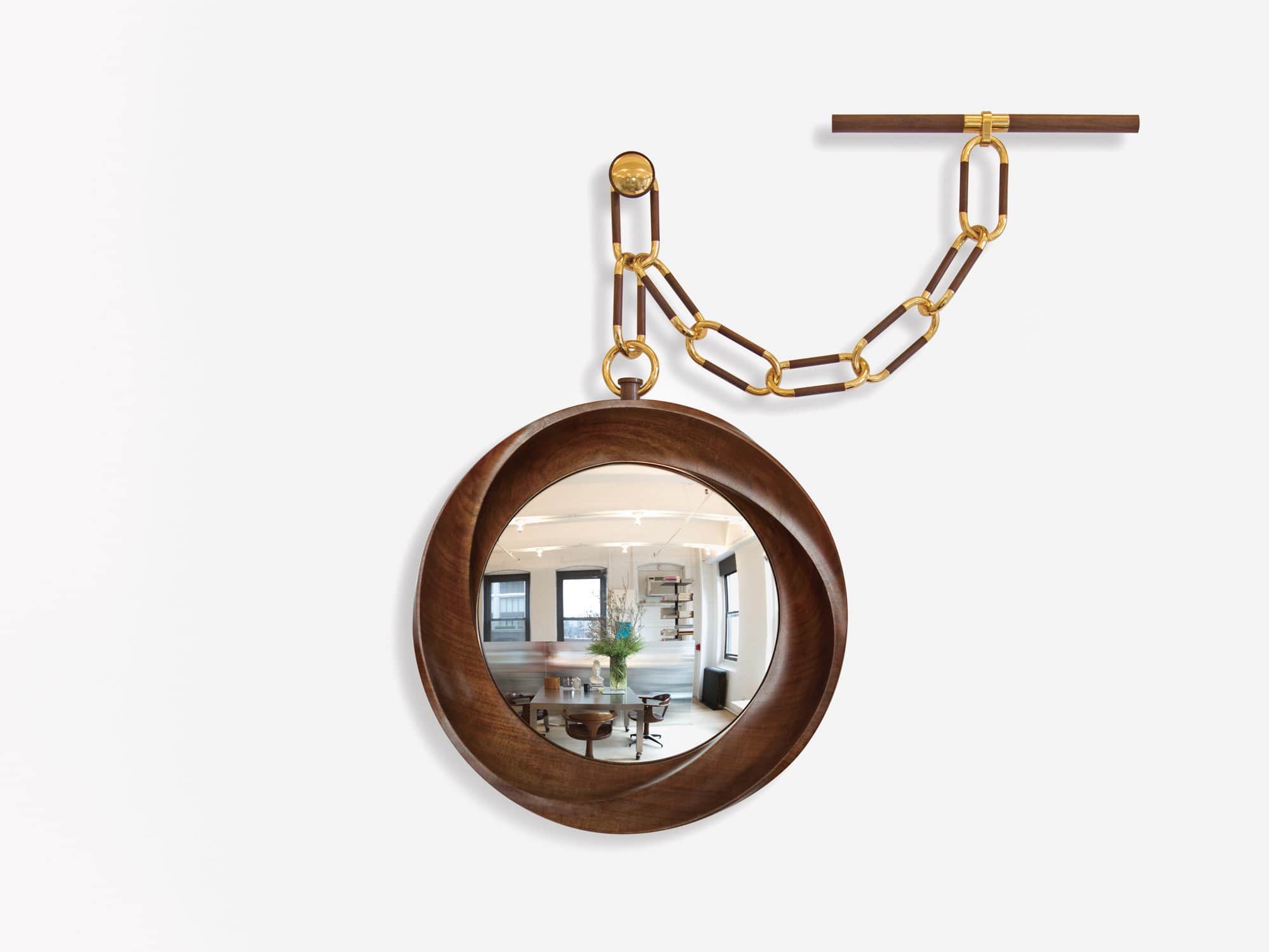 This image shows the CE09 Montre a Gousset wall mirror in a walnut finish designed by Carol Egan.  the diameter of the mirror is 18" (46cm).   Shown here against a grey background is a carved swirling wood frame convex mirror with pocket watch like decorative chain wall mounted.