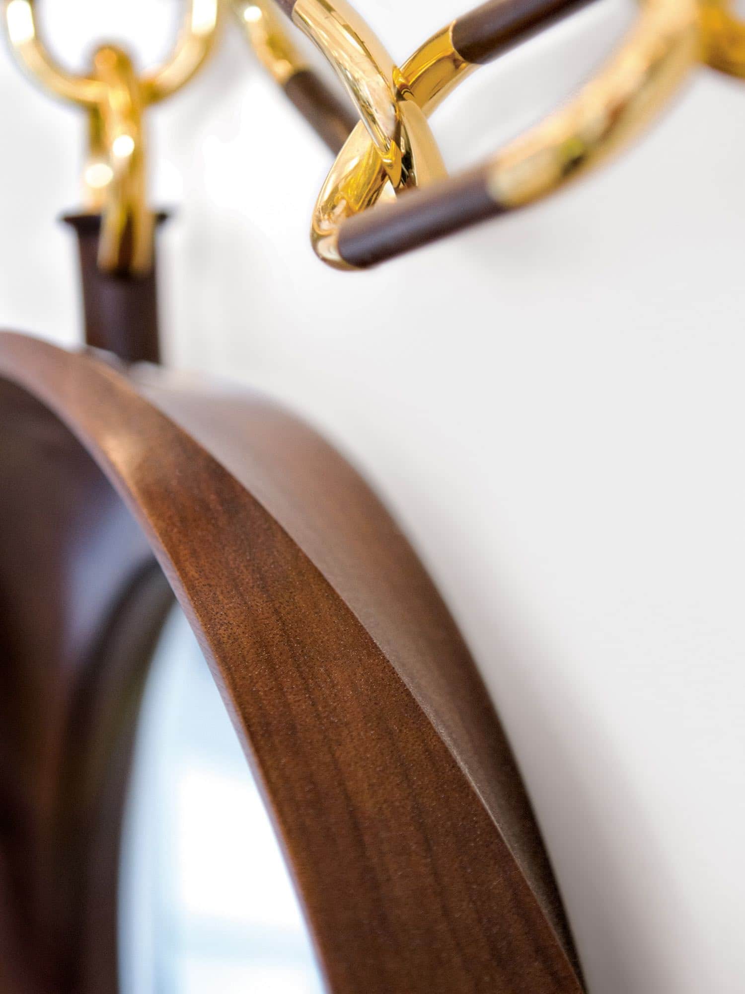 This image shows a close-up detail of the carved wood frame in walnut of the CE09 Montre a Gousset wall mirror designed by Carol Egan.  The dimensions of the mirror are 18"d (46cm).  Carved swirling wood frame convex mirror with pocket watch like decorative chain wall mounted. view detail of carving and chain in bronze.