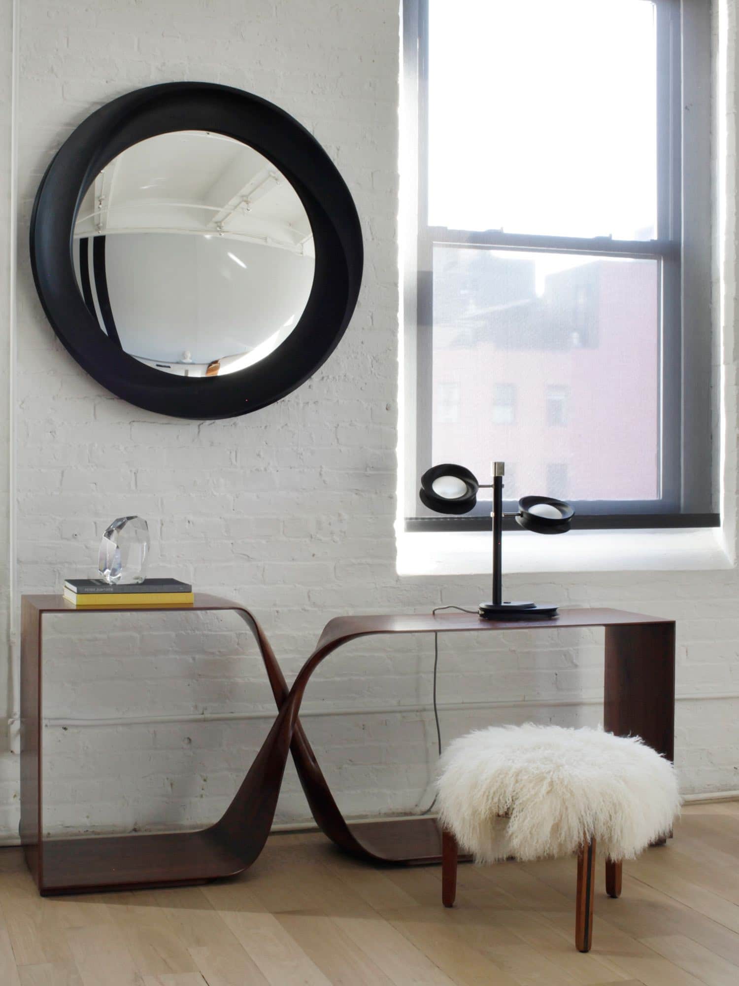 This image shows a CE10 mirror in ebonized mahogany with a convex mirror designed by Carol Egan.  The mirror is wall-mounted with a diameter of 39.5" (100cm). Shown here in the image mounted on the wall above a freestanding walnut console.  