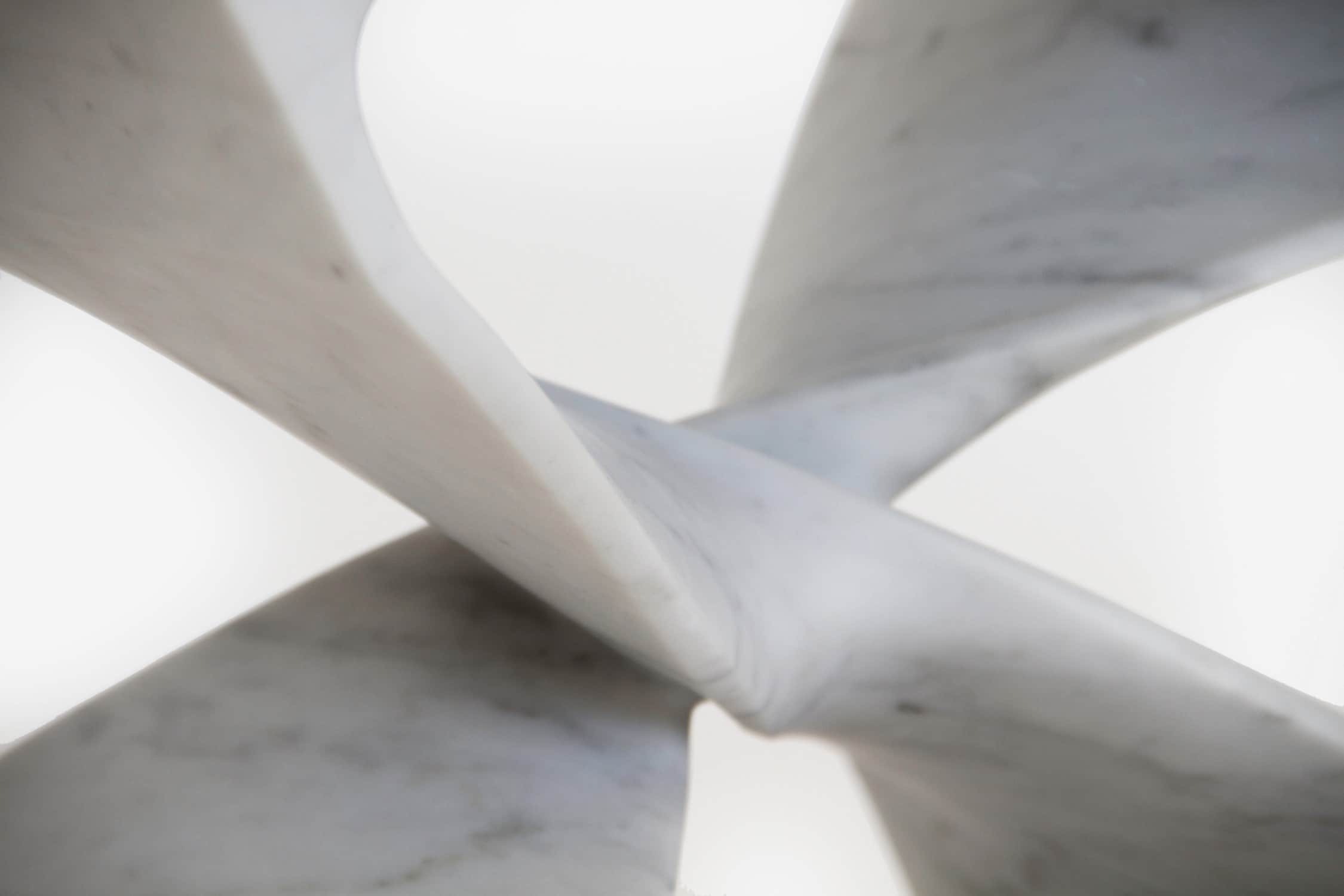 Designed by Carol Egan, this image shows a detailed close-up photograph of the carved intersections of the CE06 X Stool hand carved in Carrara marble.  The dimensions of the piece are 18"h x 22"w x 15"d (46 x 56 x 38cm).