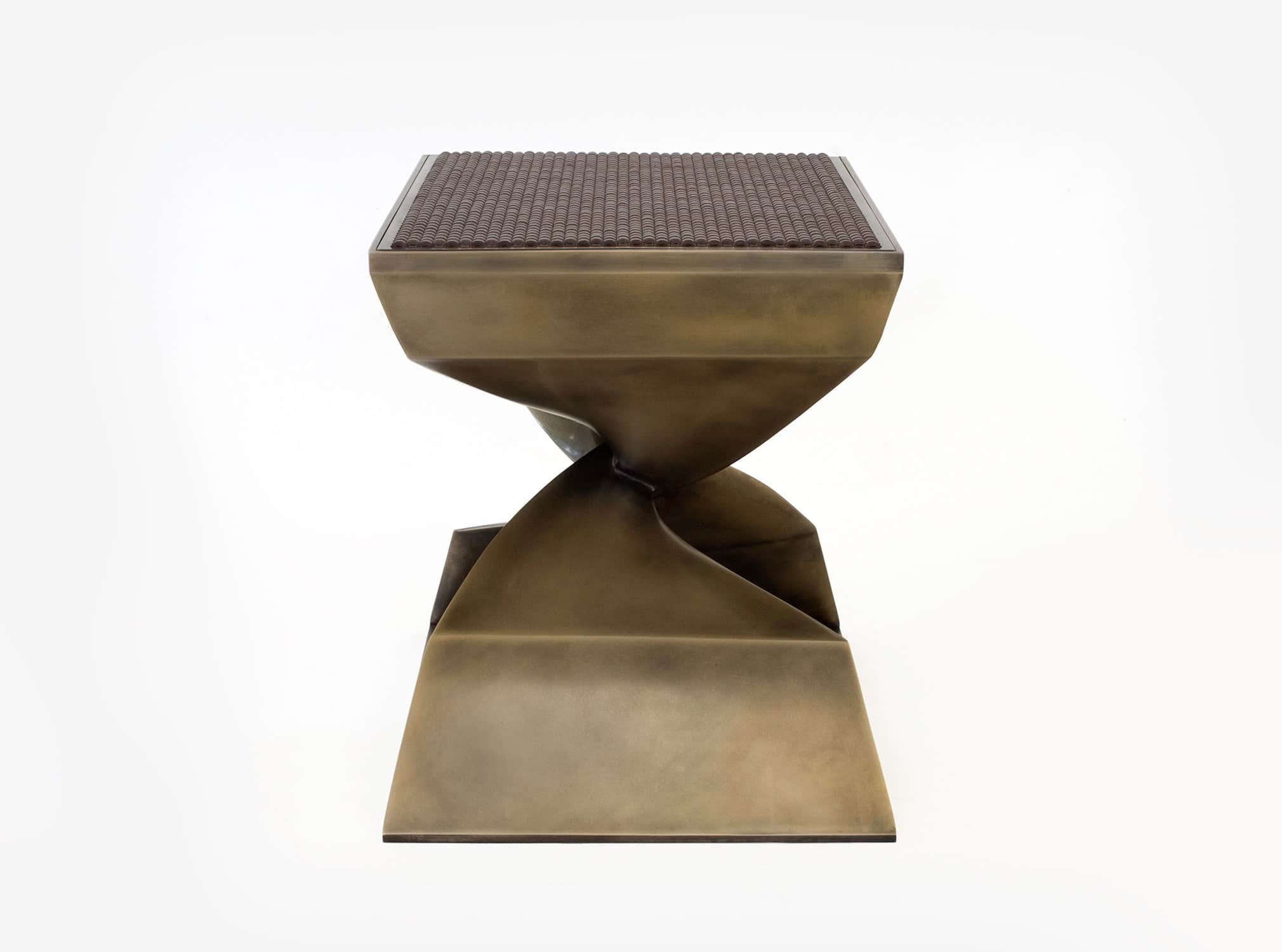 Designed by Carol Egan this image displays a side elevation view of the CE06 X Stool fabricated by a lost wax casting process.  The stool is shown here in a statuary bronze finish with a custom woven leather and metal seat top.  The dimensions of the stool are 18"h x 22"w x 15"d (46 x 56 x 38cm).