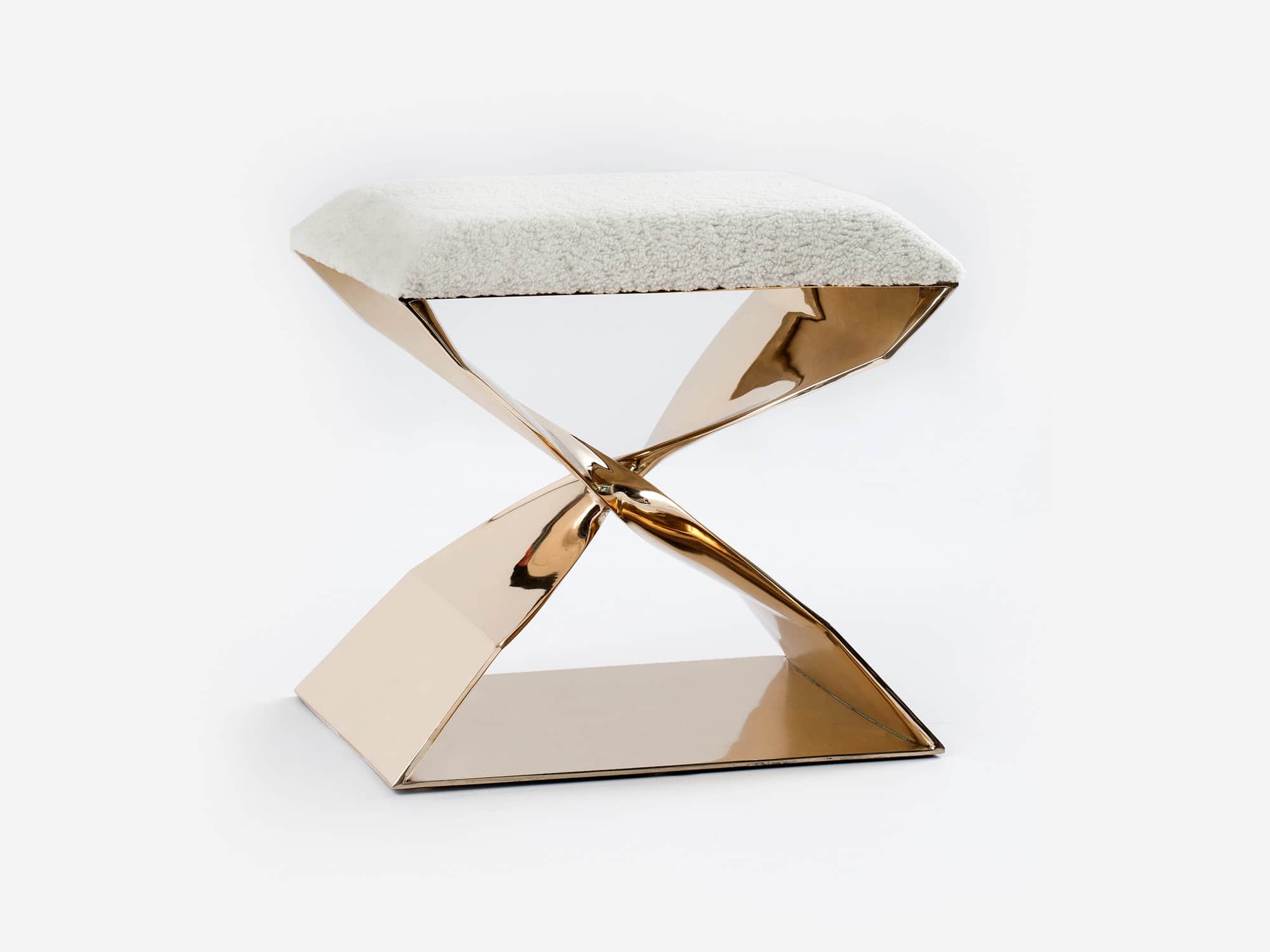 Designed by Carol Egan, this image shows a CE06 X Stool in a polished Silicon bronze finish.  The stool is Cast in Bronze and shown here with a natural shearling upholstery.  The dimensions of the piece are 18"h x 22"w x 15"d (46 x 56 x 38cm).