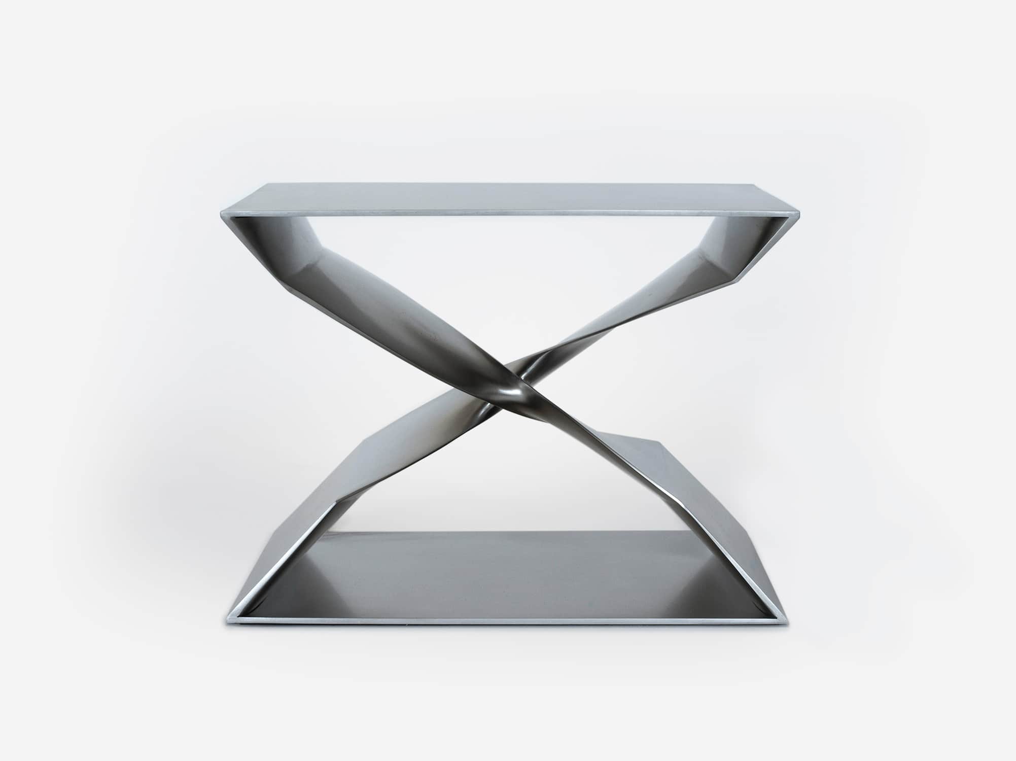 This image shows the CE06 X- Stool in a stainless steel finish designed by Carol Egan.  The Stool is a casting in steel.  Shown here against a pale grey background.  The dimensions of the piece are 17"h x 22"w x 15"d (44 x 56 x 38cm).