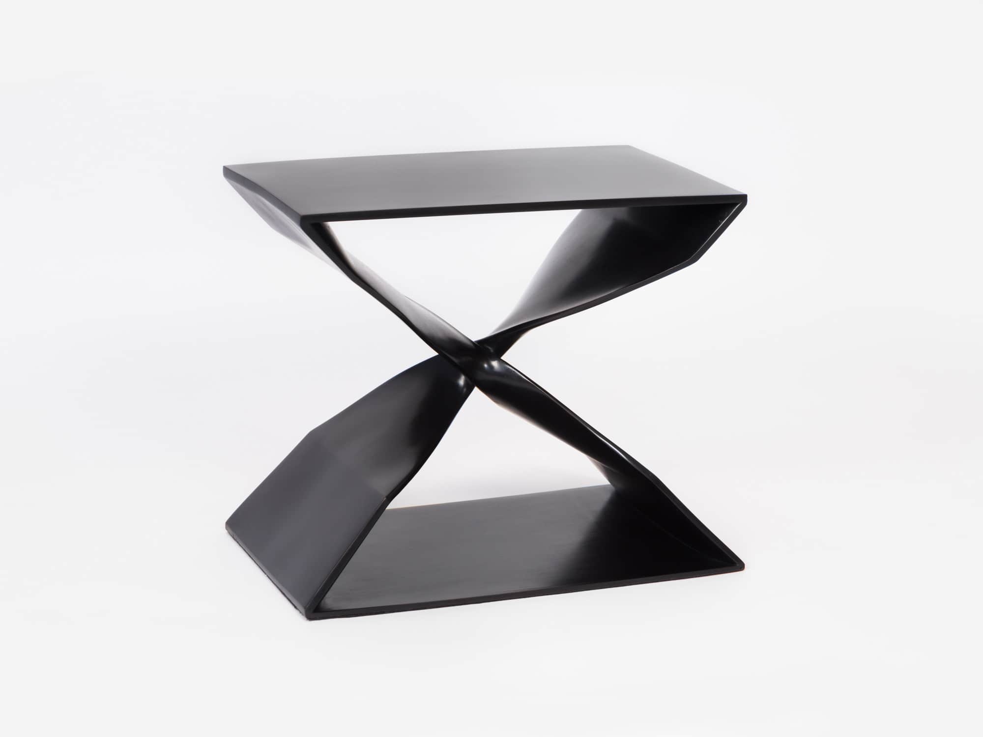 Displayed in this image is a blackened bronze CE06 X Stool designed by Carol Egan.  The stool is shown against a grey background.  The x stool is made by lost wax casting and the dimensions are 18"h x 22"w x 15"d (46 x 56 x 38cm).