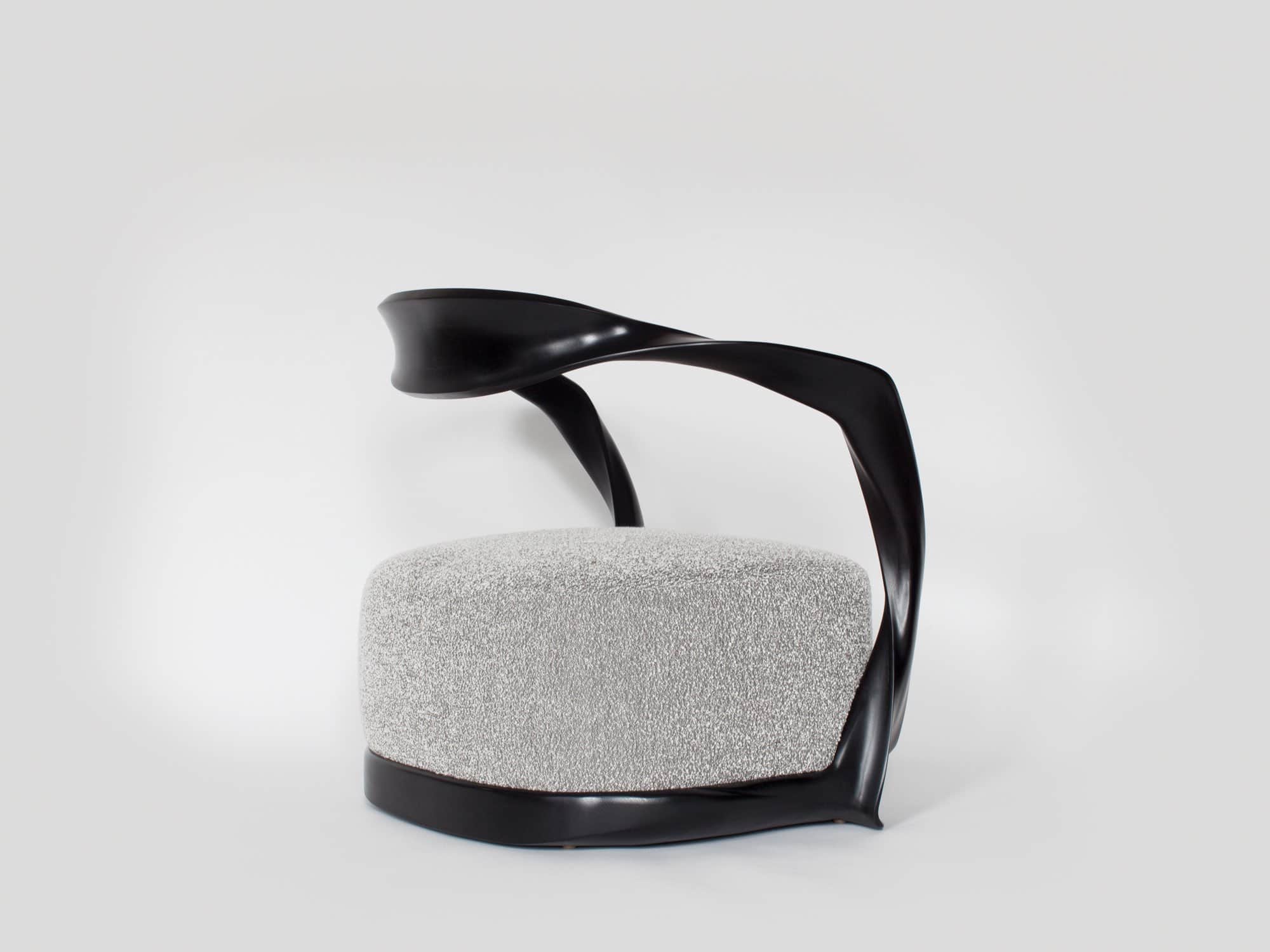 Designed by Carol Egan and shown here in a side profile is the CE15 Ombre armchair in an ebonized mahogany finish and upholstered in a custom Silk boucle fabric designed by Sam Kasten.  The dimensions of the armchair are 28"h X 32"w X 24.5"d (70 X 80 X 60cm).  The chair has a carved ribbon like frame with an open back and a sprung upholstered seat.
