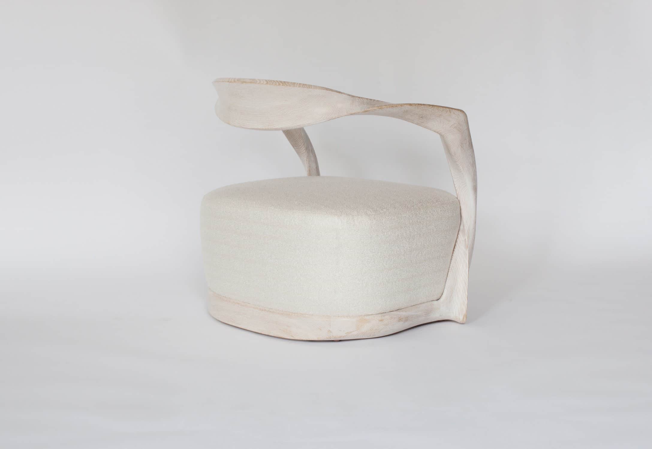 Designed by Carol Egan and shown here in a side profile is the CE15 Ombre armchair in a cerused oak finish and upholstered in a custom Silk boucle fabric designed by Sam Kasten.  The dimensions of the armchair are 28"h X 32"w X 24.5"d (70 X 80 X 60cm).  The chair has a carved ribbon like frame with an open back and a sprung upholstered seat.