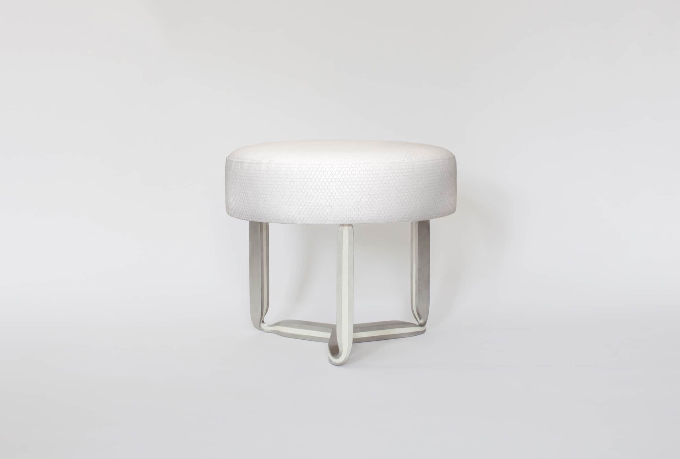 Designed by Carol Egan and displayed against a grey background, the CE17 Ottoman is shown here in a cast stainless steel and recycled white resin inlay with a custom stamped octagonal white leather seat top.  The dimensions of the piece are 17"h X 21"w X 21"d (44 X 54 X 54cm).