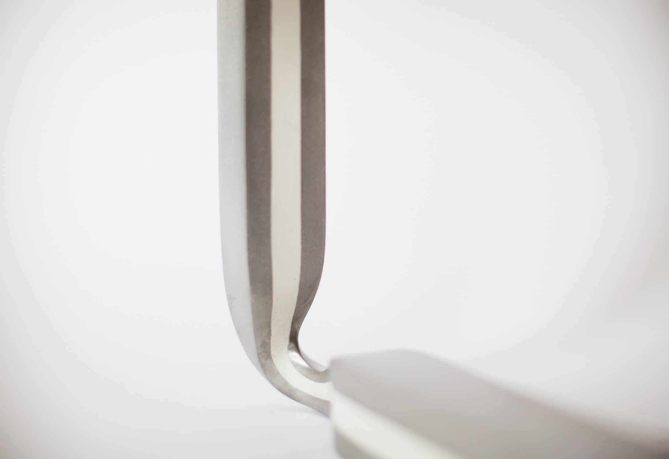 Designed by Carol Egan and displayed against a grey background, this image shows a close-up detailed view of the leg and cast metal base of the CE17 Ottoman in a stainless steel and recycled white resin inlay finish.   The seat top is upholstered with a custom stamped octagonal white leather from Capricorn Hides in Los Angeles.  The dimensions of the piece are 17"h X 21"w X 21"d (44 X 54 X 54cm)