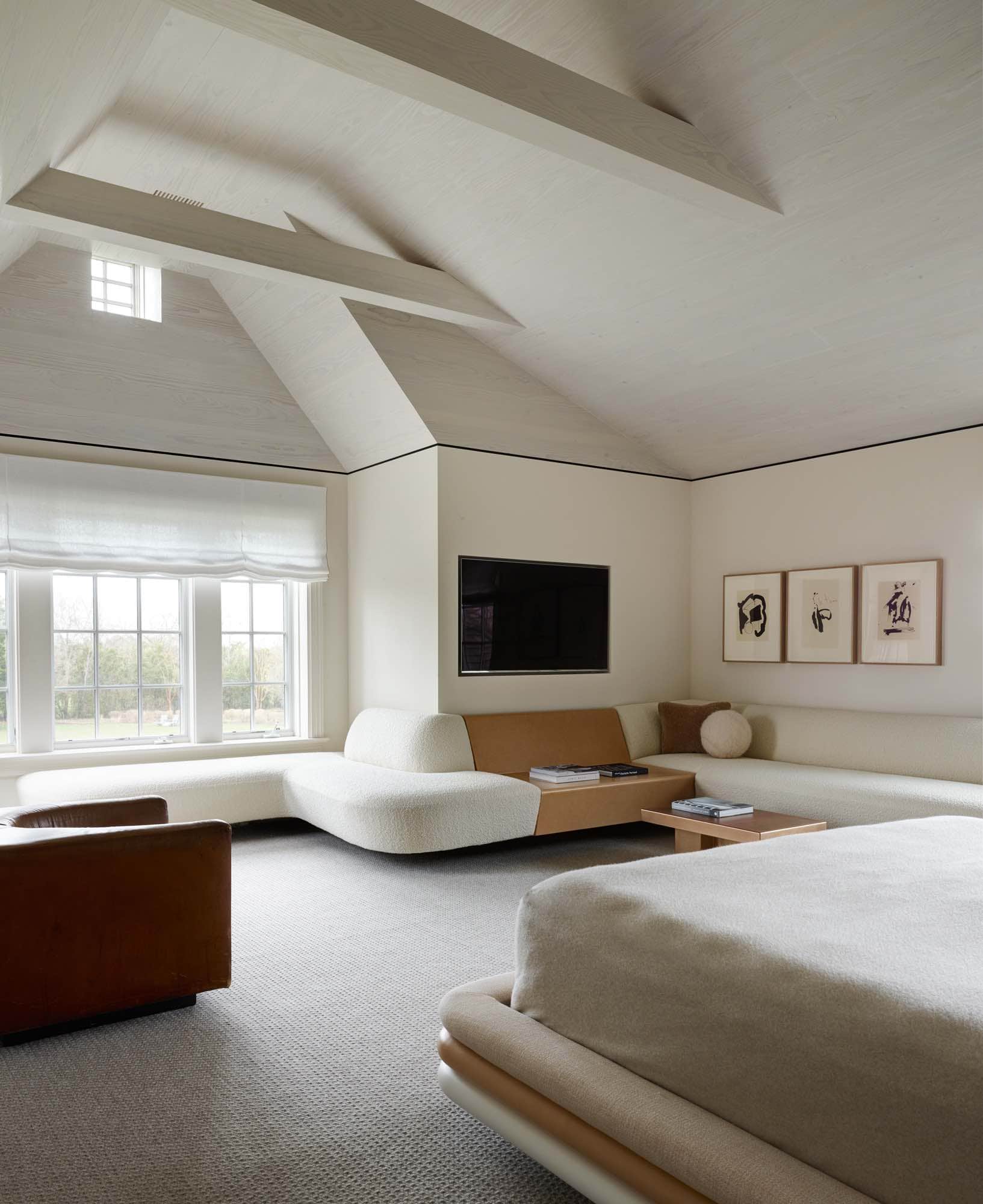 A photograph of a master bedroom designed by Carol Egan.  The custom bed design by Studio Carol Egan is upholstered in Old Rose Heathered Strie fabric by MM Design and ISEO IS16 leather by Foglizzo Leather.  Along the wall is a custom floating banquette design by Studio Carol Egan in Ivory Karakaroum fabric by Dedar Milano with a ball cushion by Pierre Yovanovitch surrounding a coffee table 80 by Marcin Rusak.  Opposite is a Elliptique armchair by Bernard Govin.  Above the banquette hangs Octavio Paz Portfolio Lithographs by Robert Motherwell.