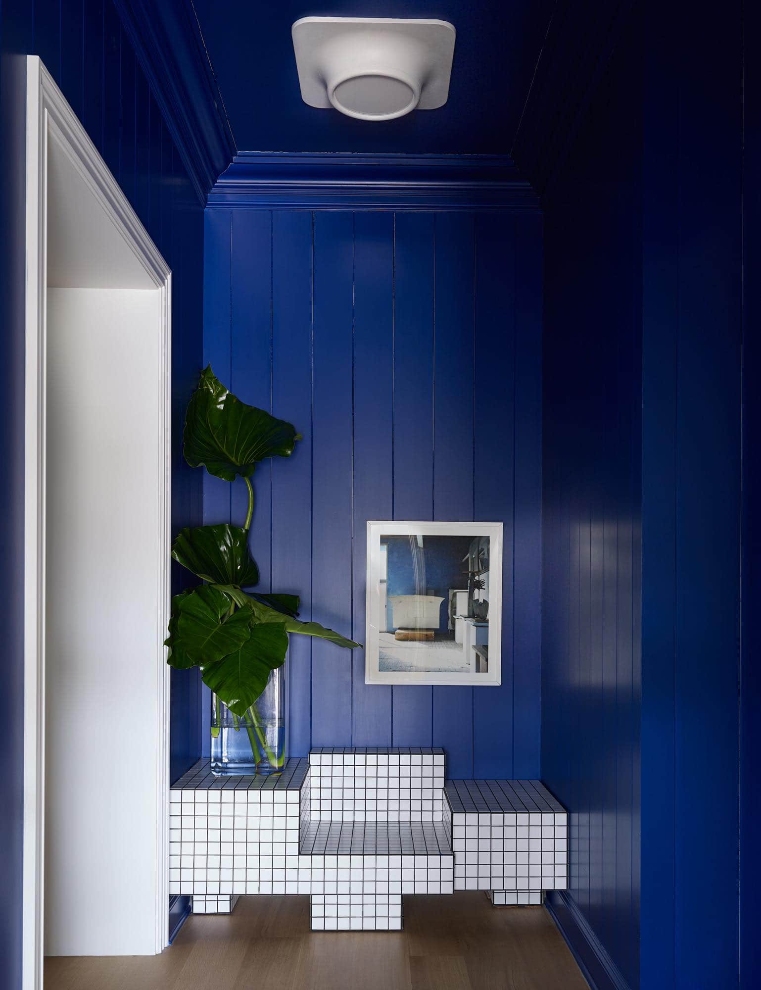 Designed by Carol Egan, this image shows the mud room paneled in a V- Groove painted wood paneled system in an ultramarine blue.  ‘Artists Handmade Houses - Constantino Nivolo’ photograph by Don Freeman hangs above a TS I tiled bench by Nima Abili that sits on plank oak flooring.  The room is lit by a 1970s vintage French flush mount ceiling light.