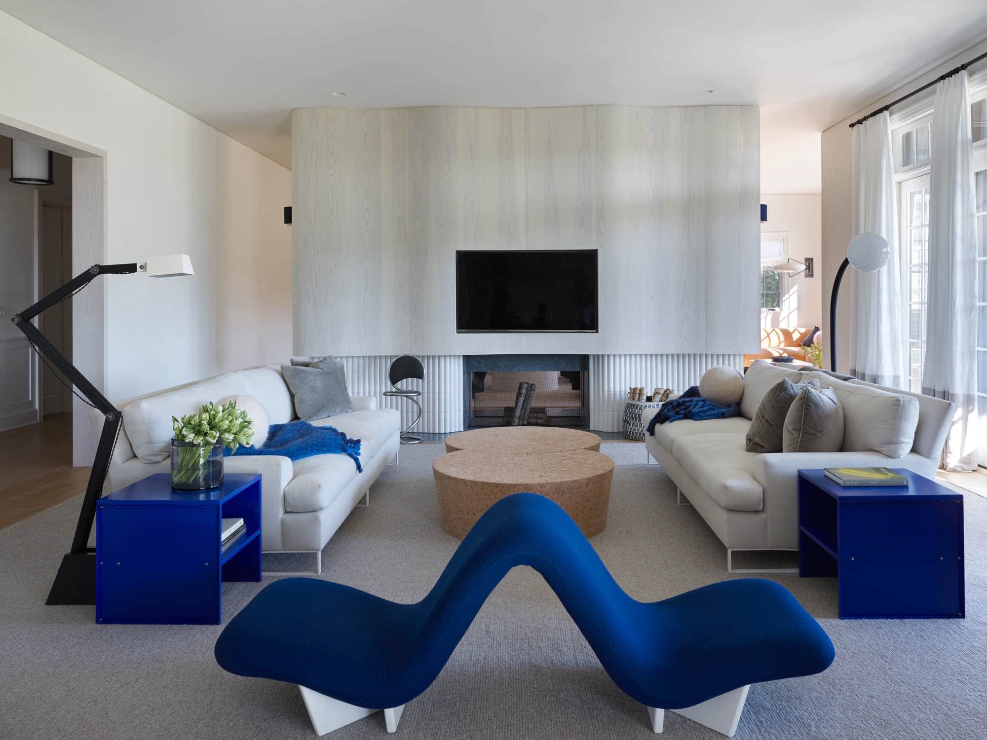 Shown here is an image of a Sagaponack residence main living room designed by Carol Egan with a Dos a Dos banquette by Pierre Paulin and Raffles sofas by Vico Magistretti in "Back to Basics Platinum" Fabric by Holly Hunt.  There are a pair of side tables by Donald Judd flanking the sofas in ultramarine blue.  The coffee table is a custom design from the Cork Series designed by Jasper Morrison.  The area rug is a Sardinian natural wool woven carpet by FJ Hakimian.  The floor lamp by Gino Sarfatti and Architect standing lamp by Florence Lopez are positioned behind each sofa.