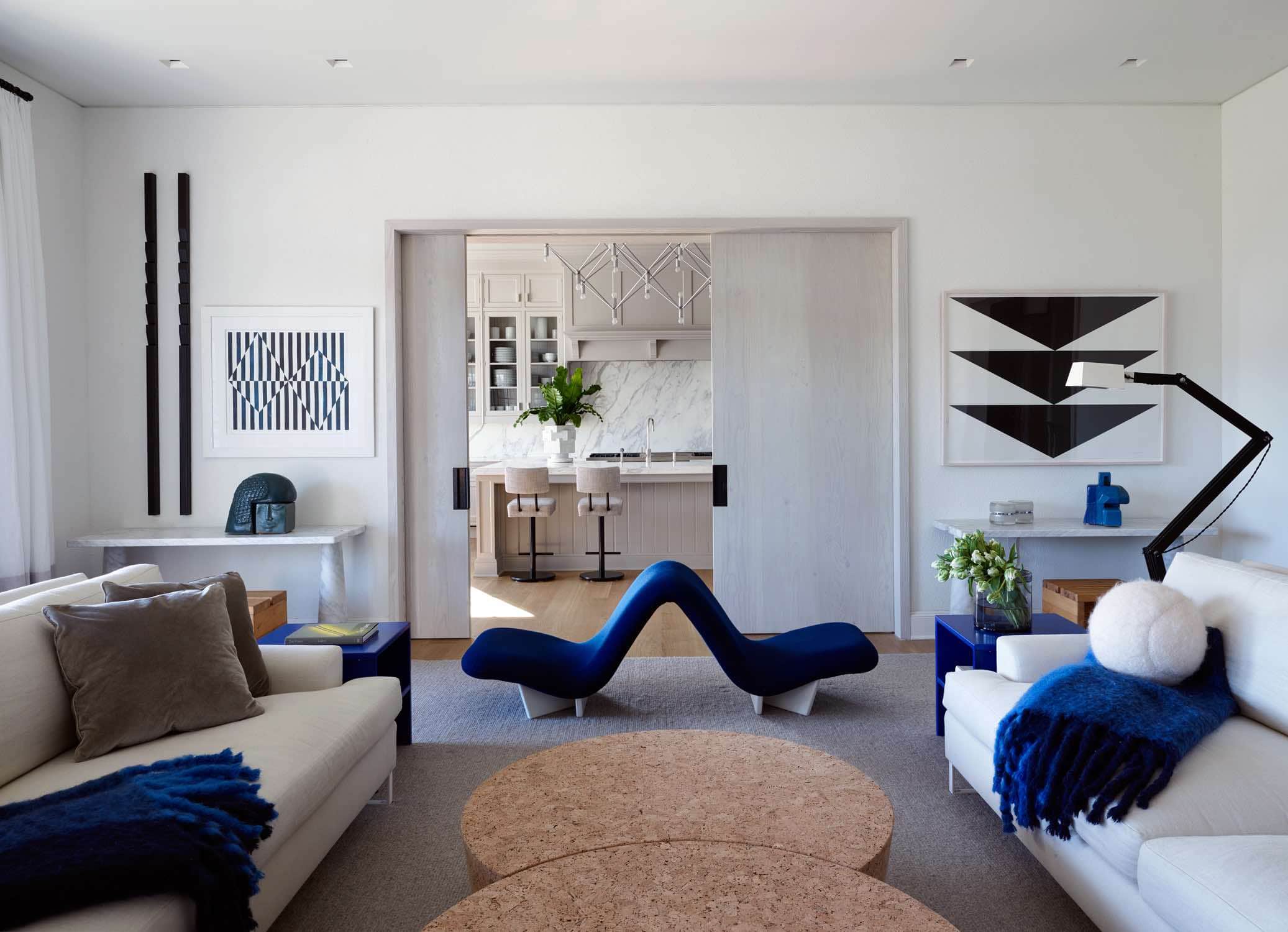 A photograph of a living room designed by Carol Egan.  The far wall consists of a pair of vertical wall lamps from RE Steele Antiques and Artwork by Carmen Herrera.  Below are sculptures by Andree and Michel Hirlet and Yo-Yo glass table lamps by Eugenio Gentile Tedesch that sit on marble console tables designed by Mangiarotti.  The Raffles sofas designed by Vico Magistretti is accessorized with an Ocean mohair throw blankets by Lena Rewell.