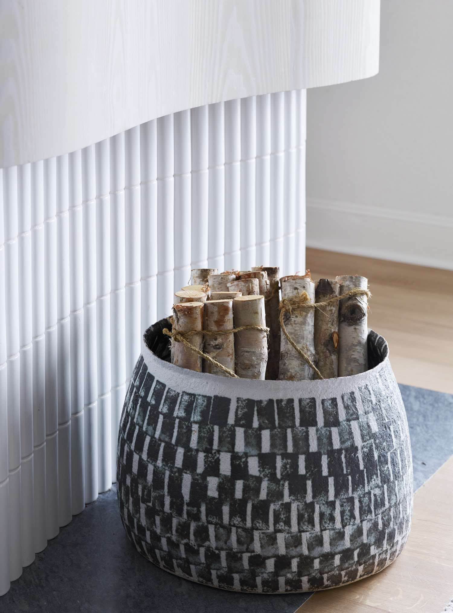 Designed by Carol Egan, this image shows a fireplace wall constructed with a undulating wall and clad in Douglas fir carved wood and SOAP ceramic tile by Kaufmann Keramik & Douglas.  Silver beech logs stored in a stoneware vase by Kati Tuominen-Niityla.