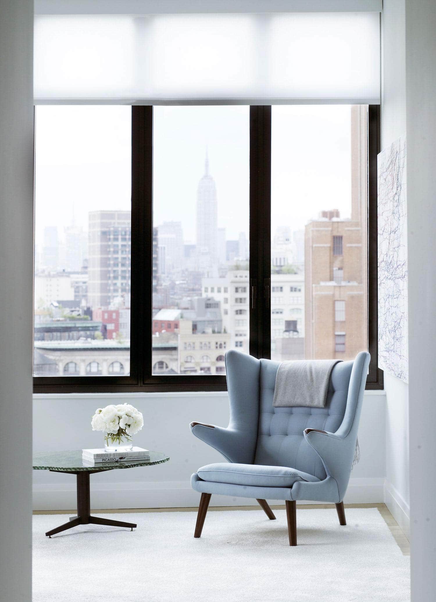 The master bedroom designed by Carol Egan Interiors in this Tribeca loft has sweeping views of the Manhattan skyline.  This image shows a Hans J. Wgner "Papa Bear" chair in a vignette with a contemporary rope chandelier by Christian Astuguevieille hangs low in the room and a unique Verre Eglomise Fontanat Arte coffee table can been seen by the chair.  Artwork is by Ghada Amer.