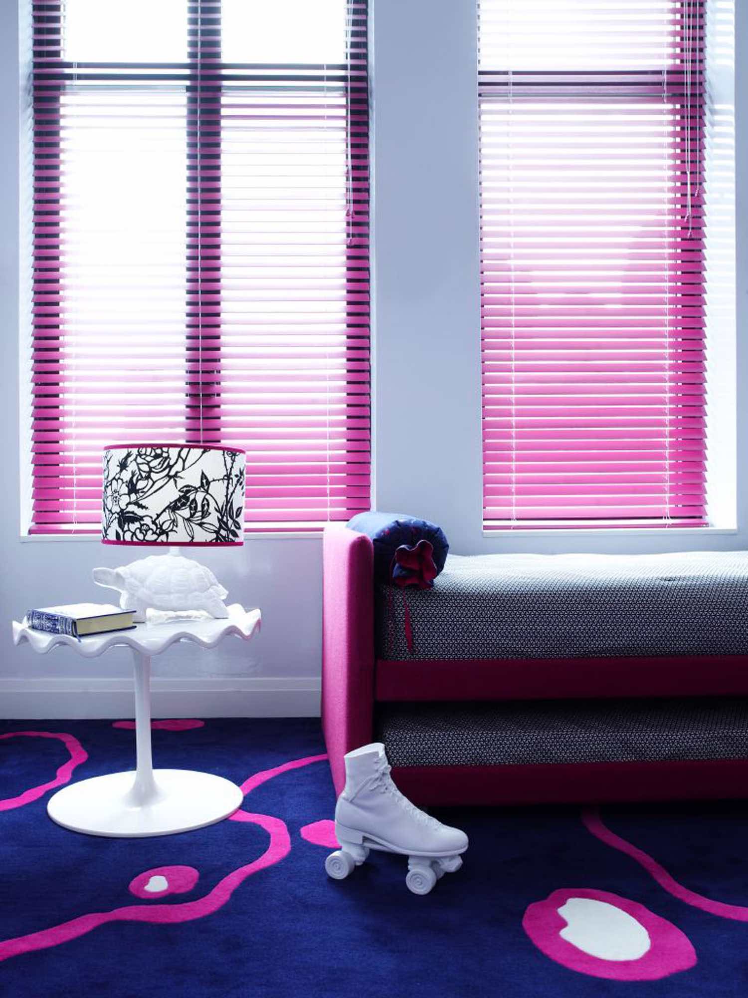 A photograph of a childs bedroom designed by Carol Egan in a Tribeca loft.  The room has a wall-to-wall custom wool and silk navy and fuschia carpet based on an art deco Ruhlmann fabric design.  Upholstered in hot pink wool is a Bliss daybed by Pinuccio Borgonovo for Flou, custom lampshade on a turtle lamp and roller skate doorstop by Areawarea.