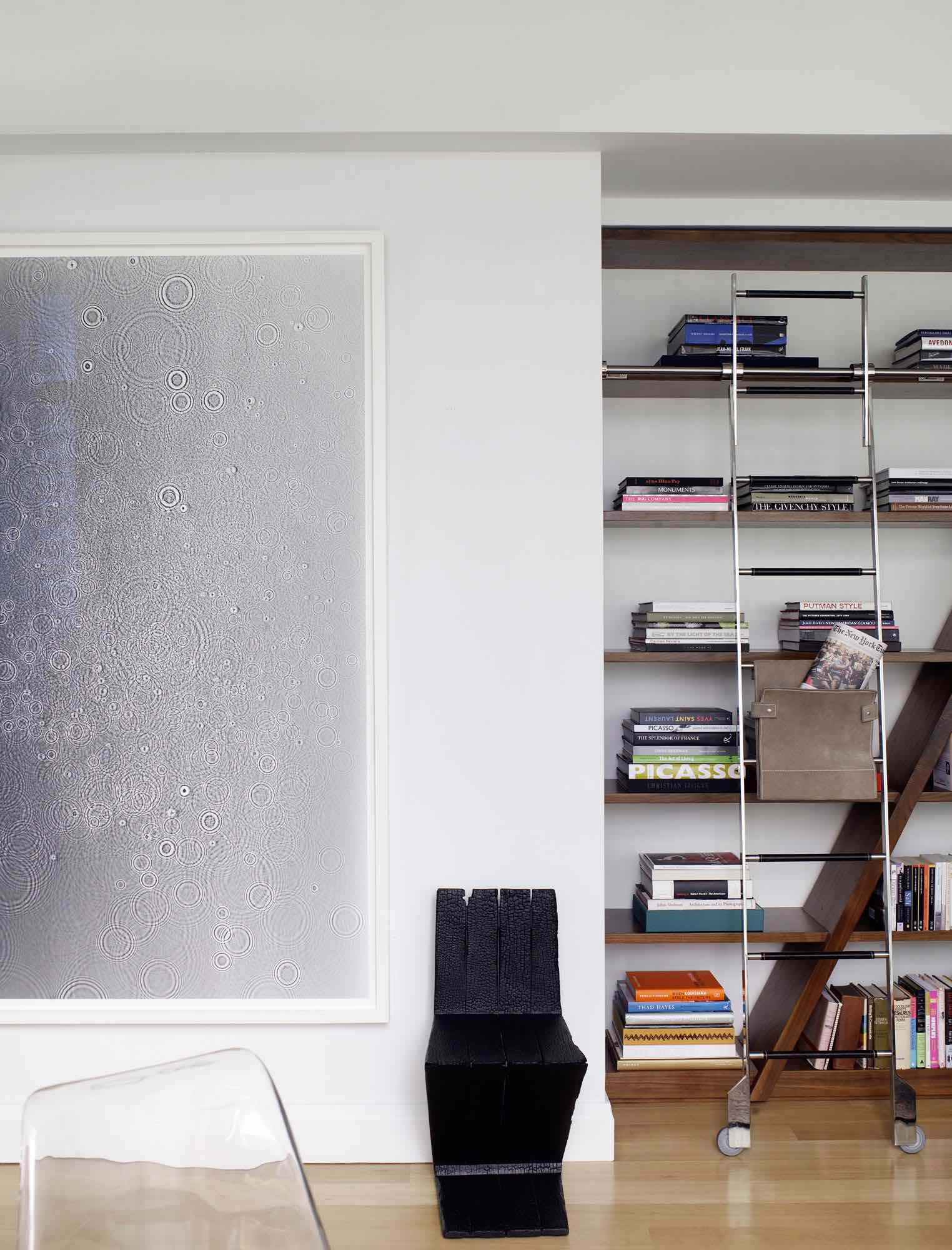 In this image of the hallway of a Tribeca loft designed by Carol Egan, a large unique gelatin Silver print photogram by artist Adam Fuss sits next to the wall of walnut library bookcases. A blackened Zig Zag Chair from "Where Theres Smoke"... by Maarten Baas stands next to the black and white artwork.