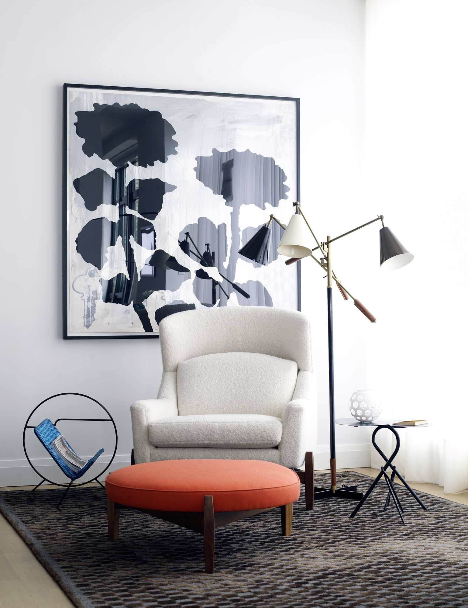 Designed by Carol Egan, this image shows a view of the library designed by Carol Egan with a chocolate brown colored silk and sisal chequerboard pattern.  Sitting on the rug in contrast white boucle fabric is the "Big Chair" armchair by Jens Risom and co ordinating round ottoman upholstered in an orange wool fabric. Propped next to the armchair is a vintage 1970s magazine table in a black metal frame with electric blue vinyl.  A large graphic black and white Donald Baechelor Painting from the Tulip series hangs on the wall beyond the chair.