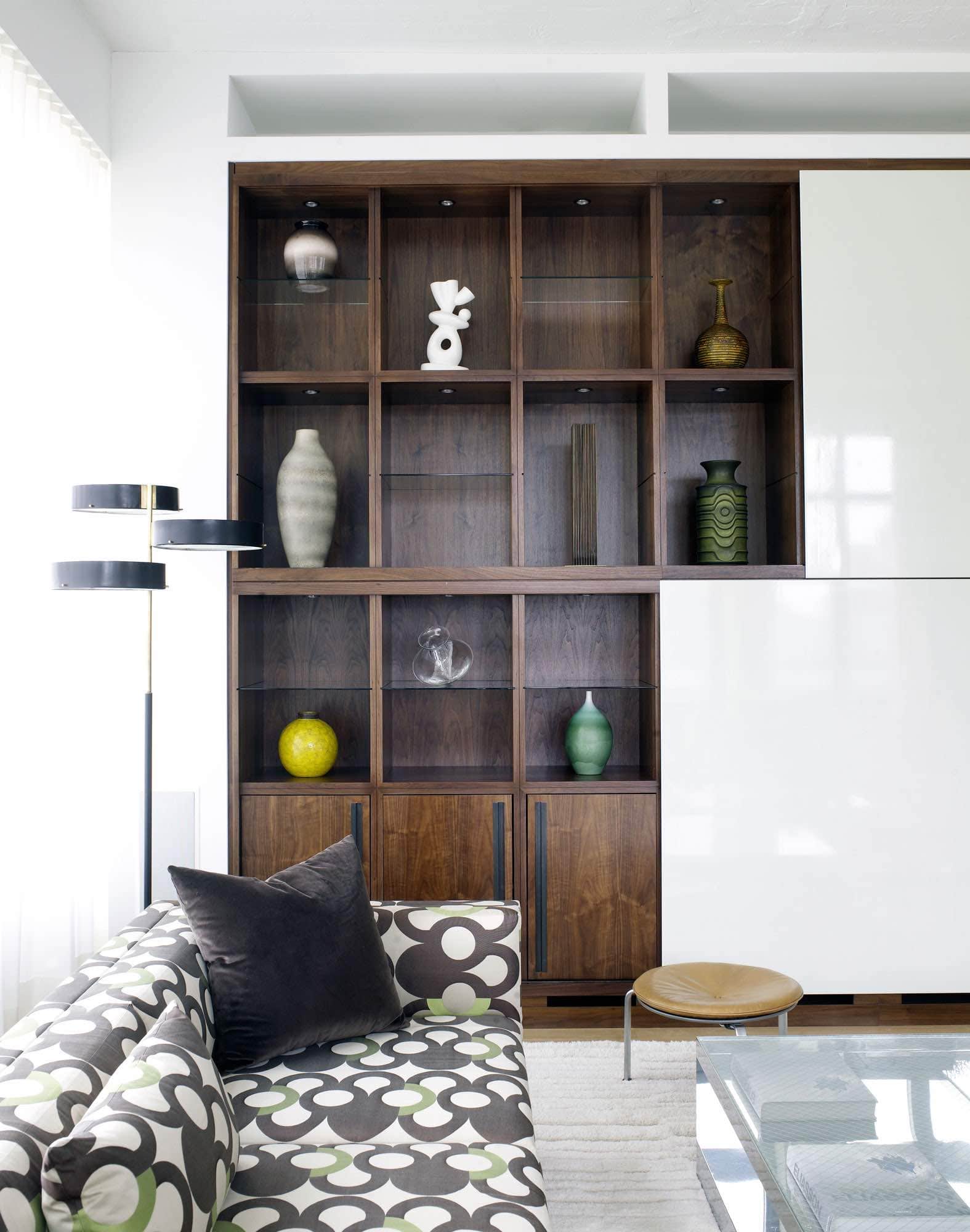 Shown in this image is a detail of the living area in a Tribeca loft designed by Carol Egan.  Cantilevered from polished steel frames are the upholstered sofa bodies wrapped in a graphic vintage Leleu fabric design from the 1950s.  Is the background is a wall of custom millwork with large sliding lacquered screens in cream to contrast with the walnut casing.  A collection of Scandinavian mid-century ceramics is on display.