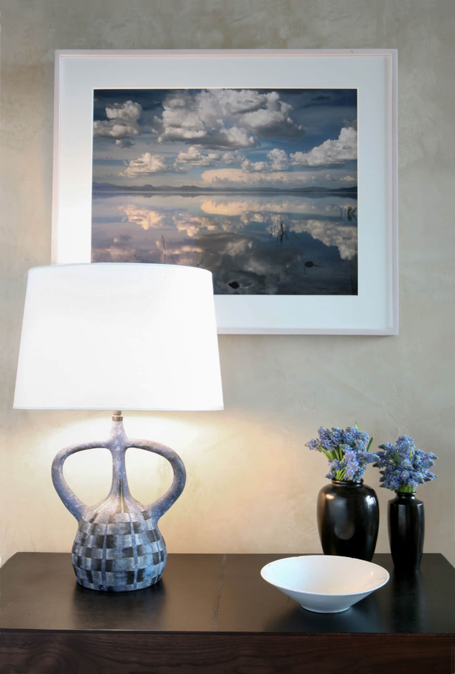 In this Aspen residence designed by Carol Egan, this image shows a detail shot of a French ceramic table lamp seen here on a wooden console table in the entry foyer with a skyscape photograph framed and hung on the venetian plaster walls.