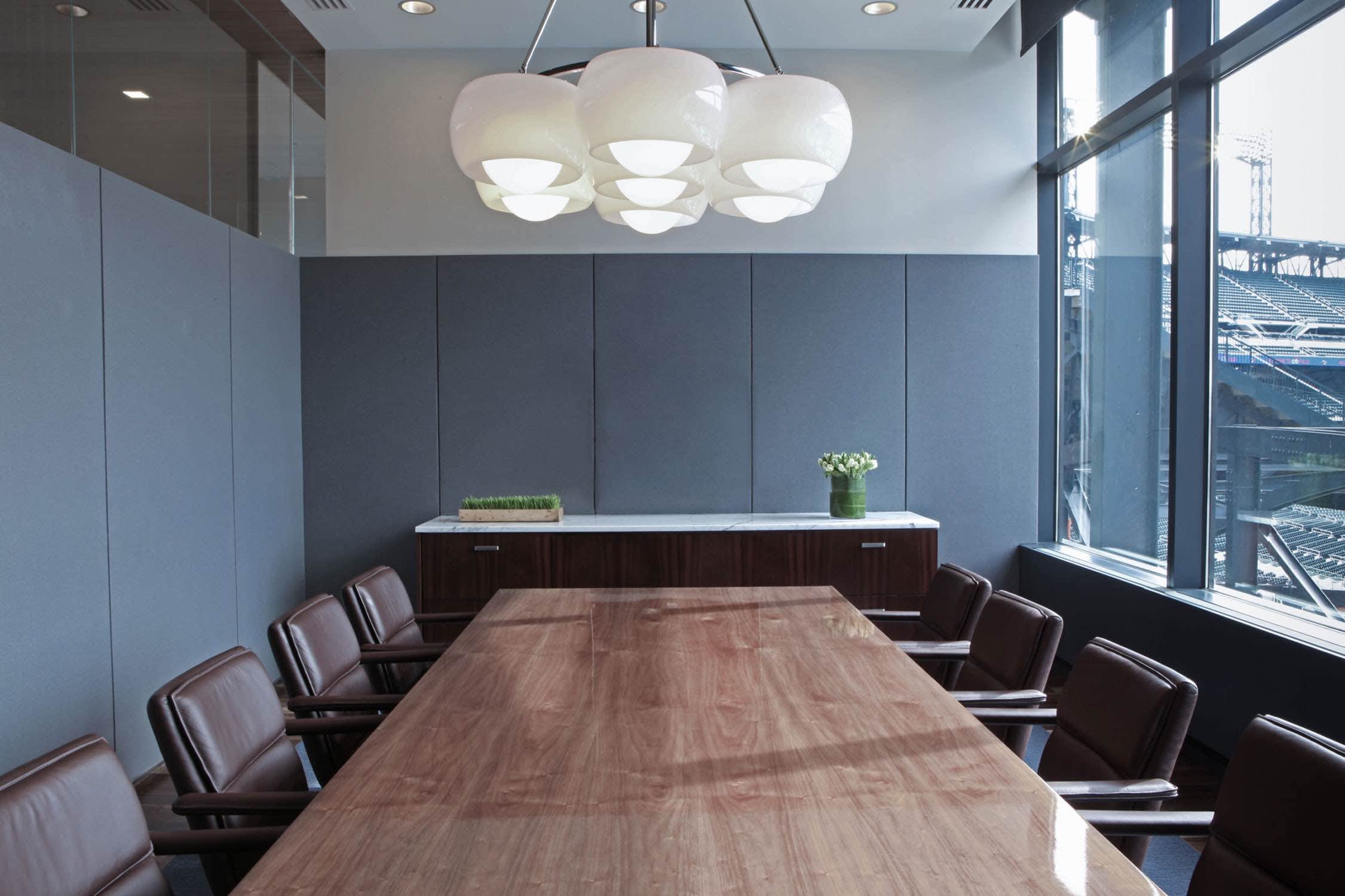 Shown here is an executive conference room at Citifield ballpark designed by Carol Egan.  The room is upholstered in Grey wool flannel on three walls with a floor to ceiling window overlooking the Citifield ballpark.  Conference table is in walnut with Eames executive management chairs in chocolate brown leather upholstery.  Five Light custom ceiling fixture in the style of Arteluce hangs on center over the conference table.