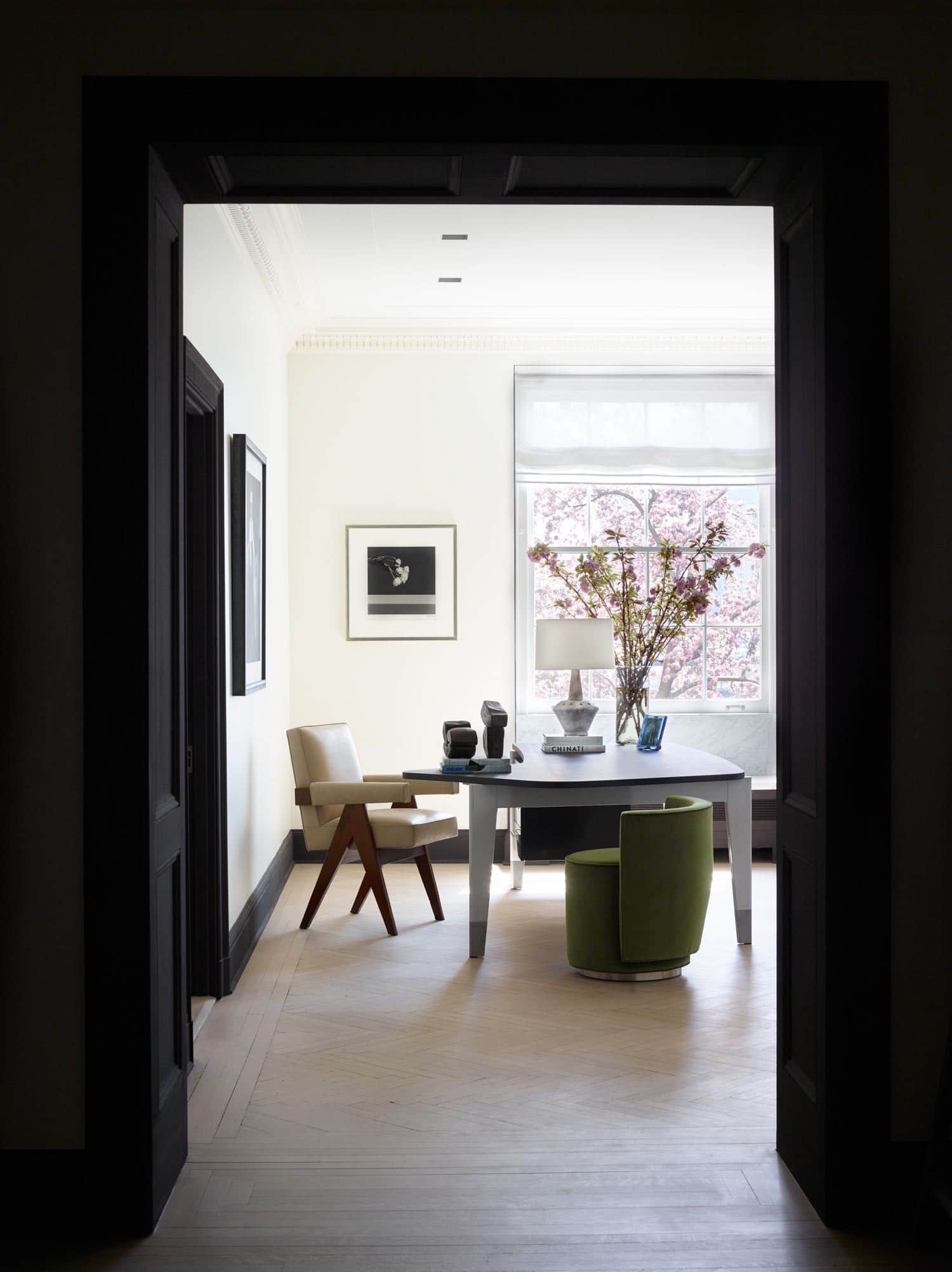 In this living room of a Sutton place residence designed by Carol Egan, a Bureau Presidence desk by Jean Prouvé displaying a ceramic lamp by Mado Jolain and sculptures by Zigor anchors the corner of the room.  Around the desk are Bond Street chair by Yabu Pushelberg and leather armchair by Pierre Jeanneret.  Steel window jambs with ribbed inlay flank all the windows which overlook the garden on the East river in New York city.