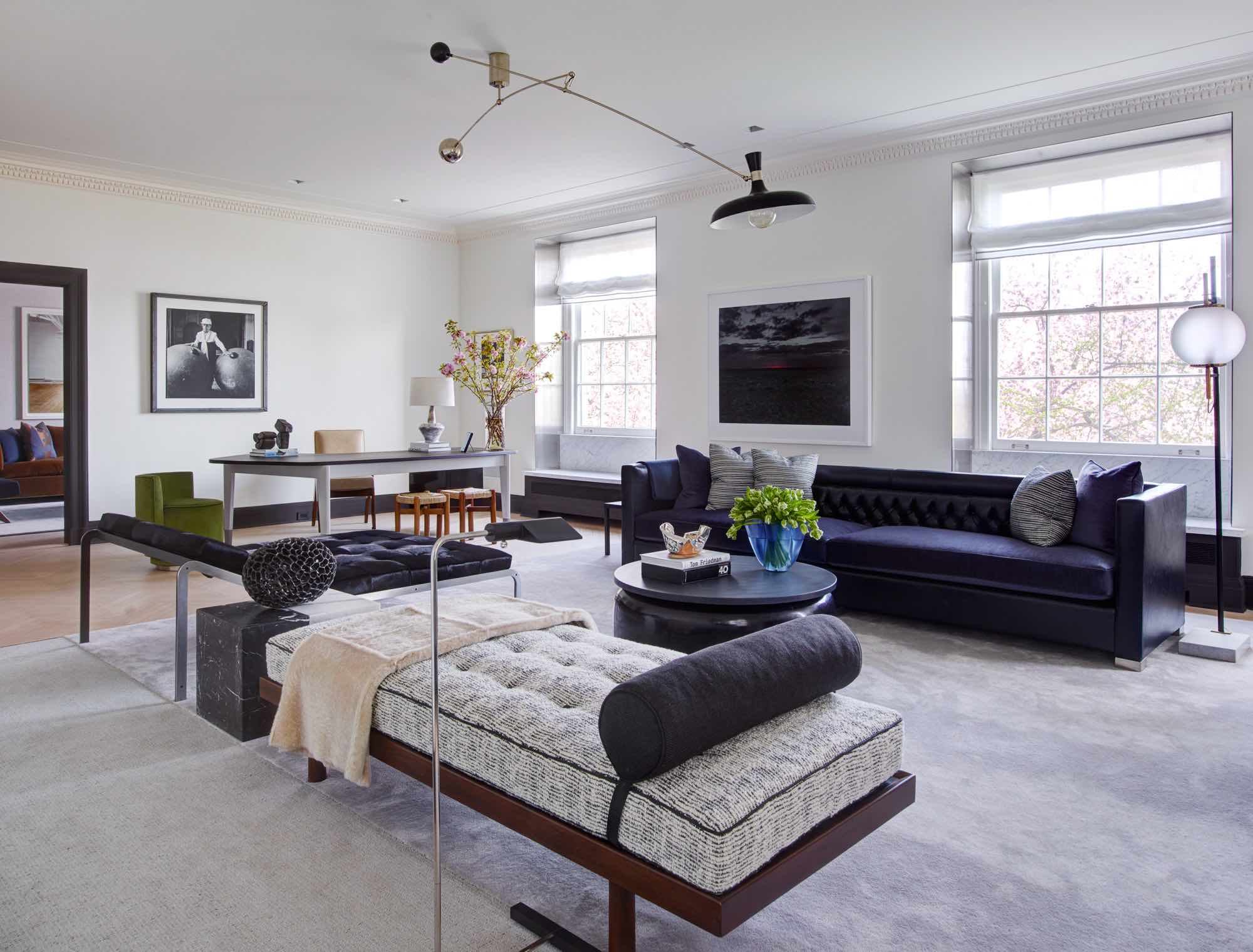 This image shows a view of the living room with custom sofa design by Carol Egan, Simple daybed by Charlotte Perriand and double day bench in the style of Pierre Paulin flanking a Bracelet coffee table by Eric Schmitt and Ceramic side table by Marianne Vissiere.  A Dust Series artwork by Nadav Kander is showcased on the window wall.  The room is lit by a Mobile hanging light by Fedele Papagni.  TA custom designed area rug with wool and silk by V’Soske Carpets delineate the sitting area in the room.