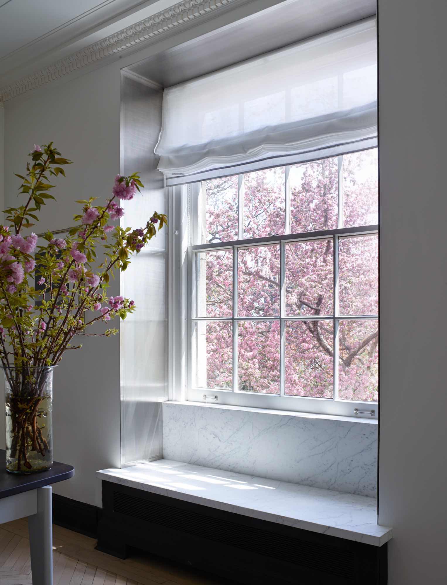 Designed by Carol Egan, this image shows Steel Window Jamb with inlaid ribbed design which flanks all the windows in the living room of this Sutton Place residence in New York.  Cherry blossoms are seen in the garden beyond.