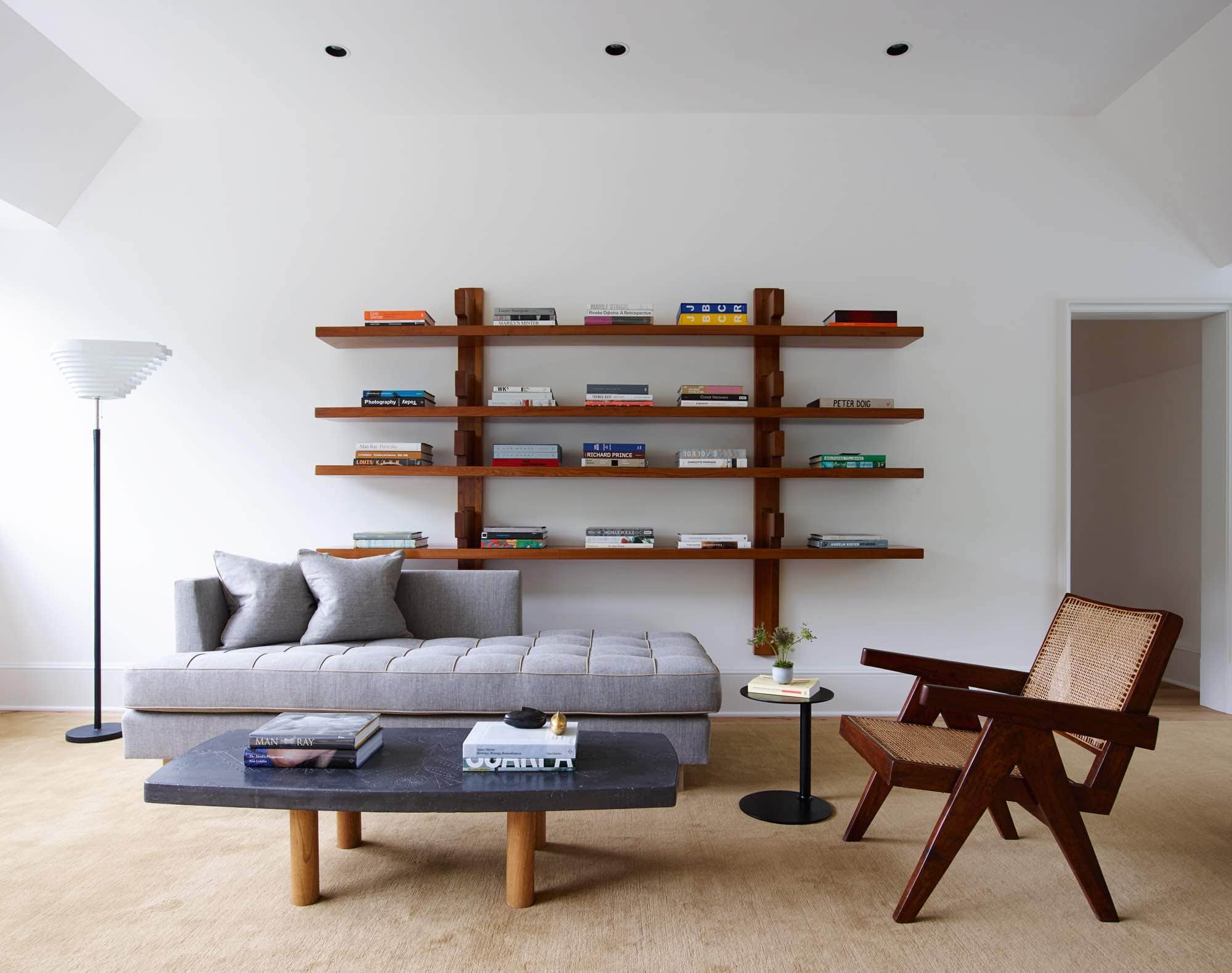 This is an image of the upstairs sitting room designed by Carol Egan.  The Ciranda side table by Ricardo Fasanello sit between a custom daybed design by Studio Carol Egan and an “Easy Armchair” by Pierre Jeanneret.  In the center is a coffee table by Roger Capron with oak legs and a ceramic tiled top.  A 1967 B17 Longue bookshelf by Pierre Chapo in oak hangs above the daybed with a collection of Art coffeee table books on display.  A camel-colored area rug by Sam Kasten anchors the room.