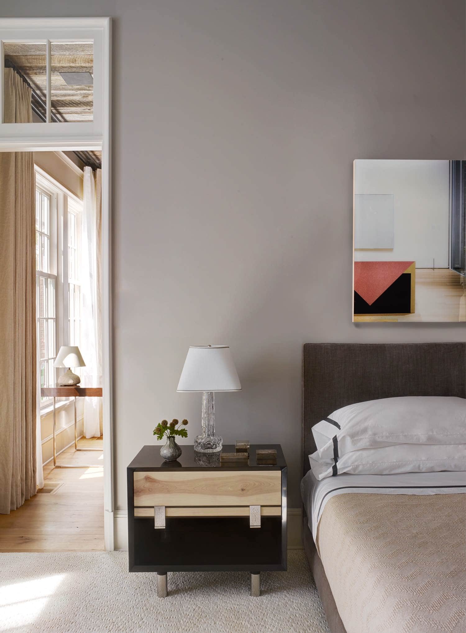 Shown here is a detail photograph of a custom silk velvet upholstered bed in the master bedroom of this Greenwich residence designed by Carol Egan.  The room is painted a soft Dior gray and the silk velvet headboard is a deeper shade of grey.  Bedside tables are by BBDW in a lacquered and pine wood finish with contrasting blacked bronze hardware. Swedish Orrefor glass bedside table lamps are seen with custom white linen shades.