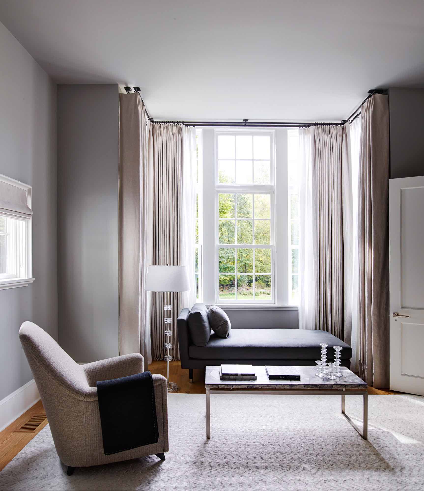 Detailed in this image is a view of the master bedrooms sitting area in a Greenwich residence designed by Carol Egan.  A custom chaise with exposed wood & nickel sabots by Doreen Interiors in Burnished Canvas Aspie Ollie rug by Mitchell Denburg sits right by the window together with a vintage marble top & nickel abase coffee table, a 1940s French high back lounge chair and a glass standing lamp RD1990 by Carl Fagerlund Orrefors illuminates the area.