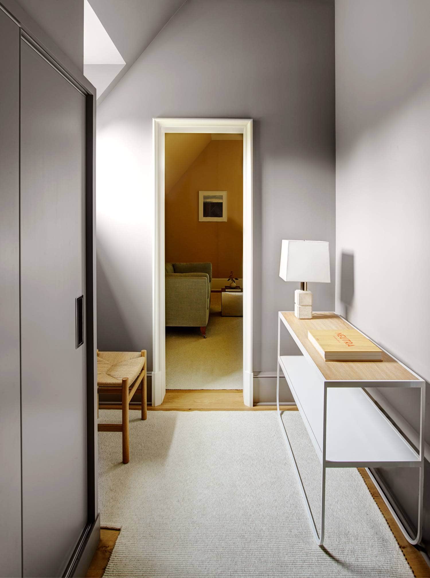 A photograph of a guest room vestibule designed by Carol Egan on the 2nd floor of a residence in Greenwich Connecticut.   The room consist of a "Rush Seat Chairs" by Charlotte Perriand on a Swiss Lace wool area rug by Mitchell Denberg.  A two tier painted metal console from Copenhagen flanks the painted grey walls.