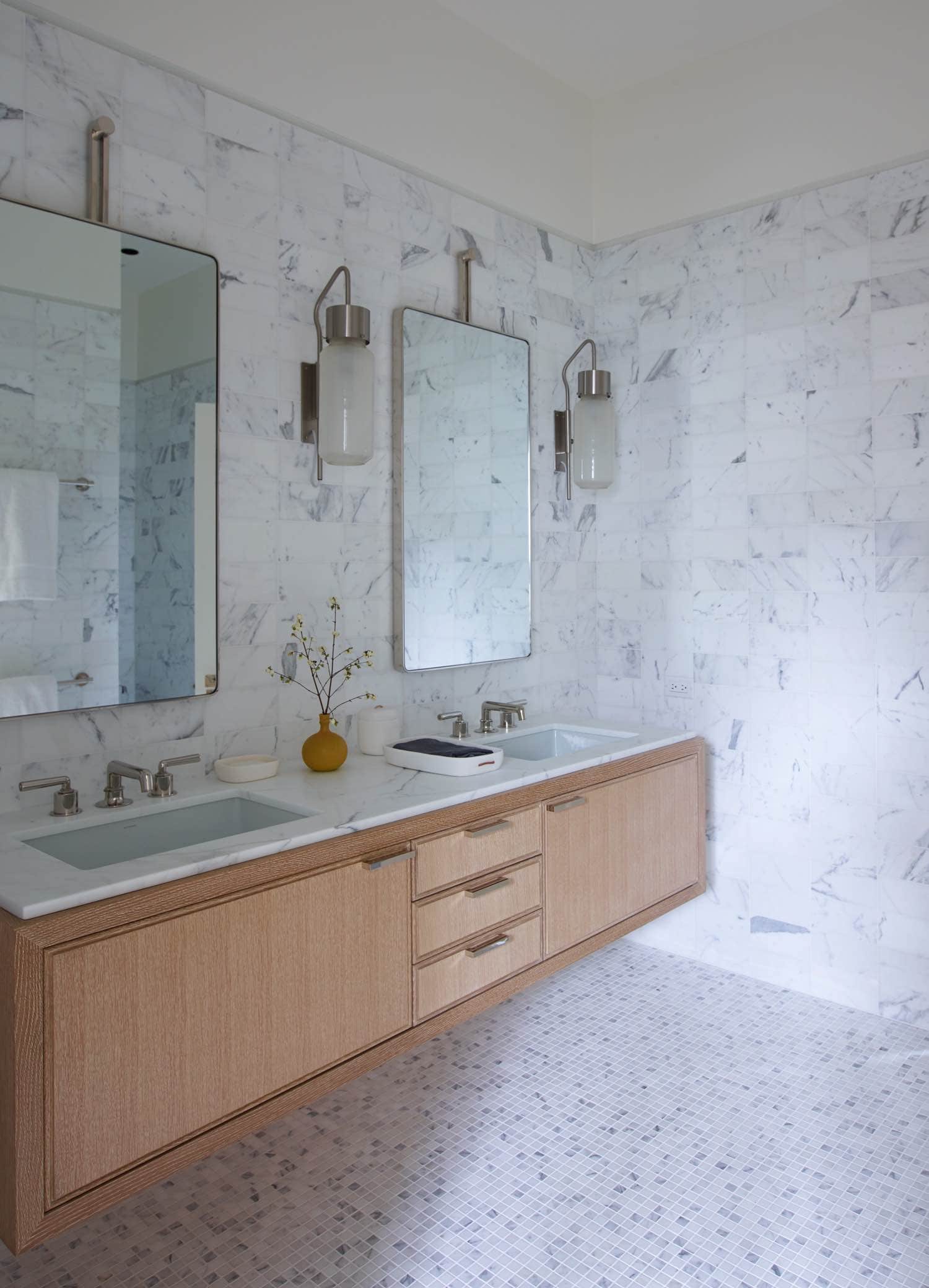 An image of a guest bathroom designed by Carol Egan in a Greenwich residence.  It is accessorized with pinion soap dish & container by Waterworks and contemporary glazed porcelain vase by Valerie Hermans.  Staturary Marble walls and mosaic floors are contrasted with rift white oak millwork for the cantilevered vanity.