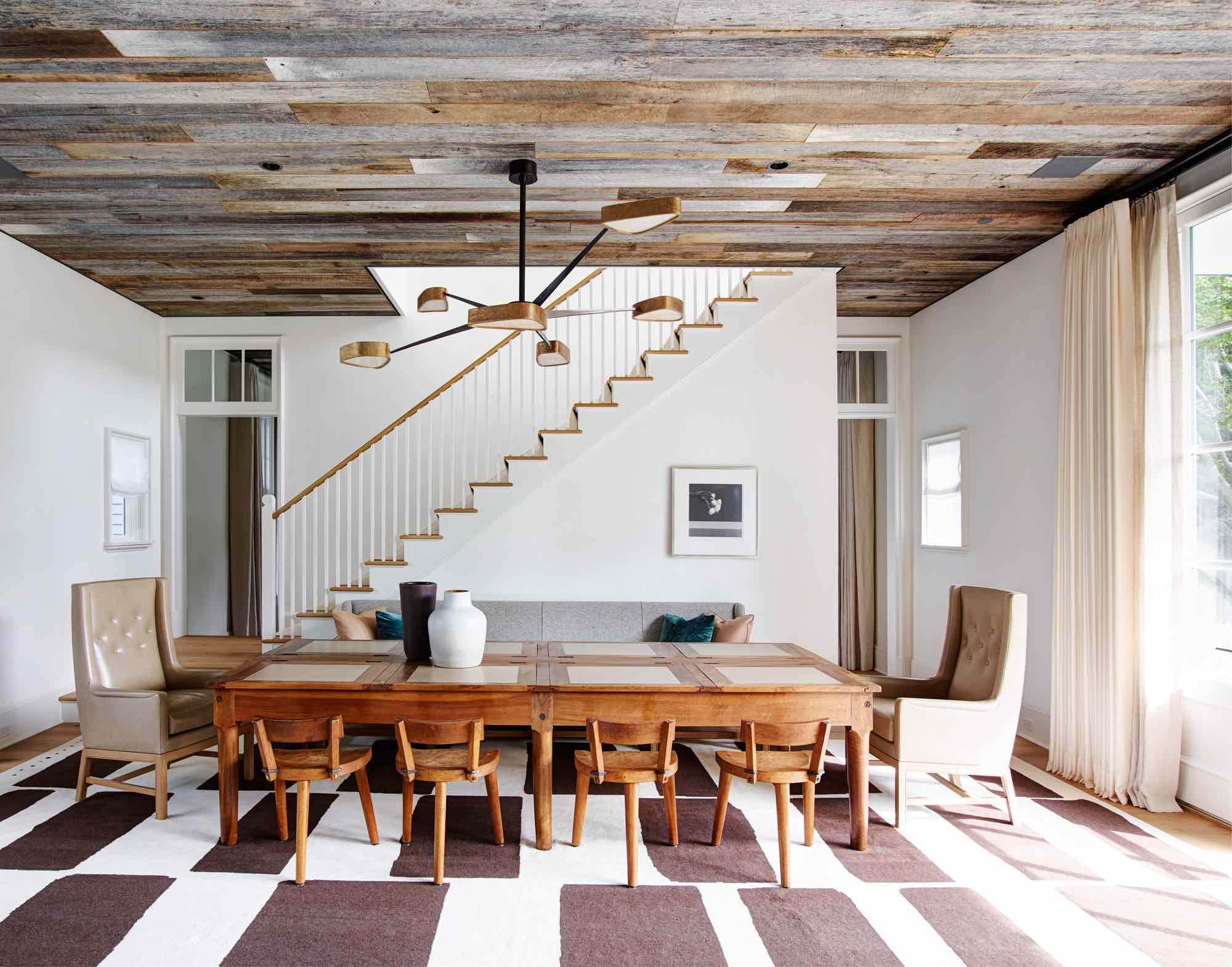 Designed by Carol Egan, this image captures the staircase and seating area in the living room.  The Custom Scanivian styled settee flanks a 19th Century Bankers Table with inset leather panels.  There are a pair of armchairs by Heige Vastegaard Jensen at each end of the long bankers table.  Carved wooden oak side chairs by Marolles from the 1950s surround the table.  The Five arm bronze and onyx chandelier is from Achille Salvagni hangs above and a frame photograph from Mapplethorpes flower series hangs low on the plaster wall above the settee.