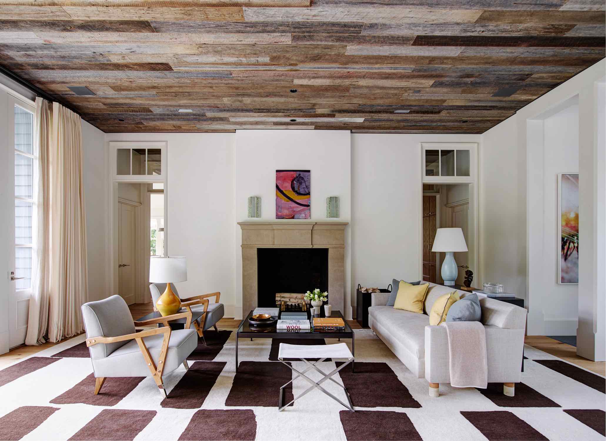 A photograph of the great room adjacent to the front entrance designed by Carol Egan with custom Sofa designed by Studio Carol Egan, Charles Club chairs by Studio Van den Akker.  Custom Lugano coffee table by Holly Hunt in the center.  Swedish stoneware vase lamp by Edwald Dahlskog, yellow-orange ceramic table by Suzanne Ramie Madoura and 1950s Fontana Arte Italian wall sconces hanf above the limstone Marble with a painting by Julian Schabel.