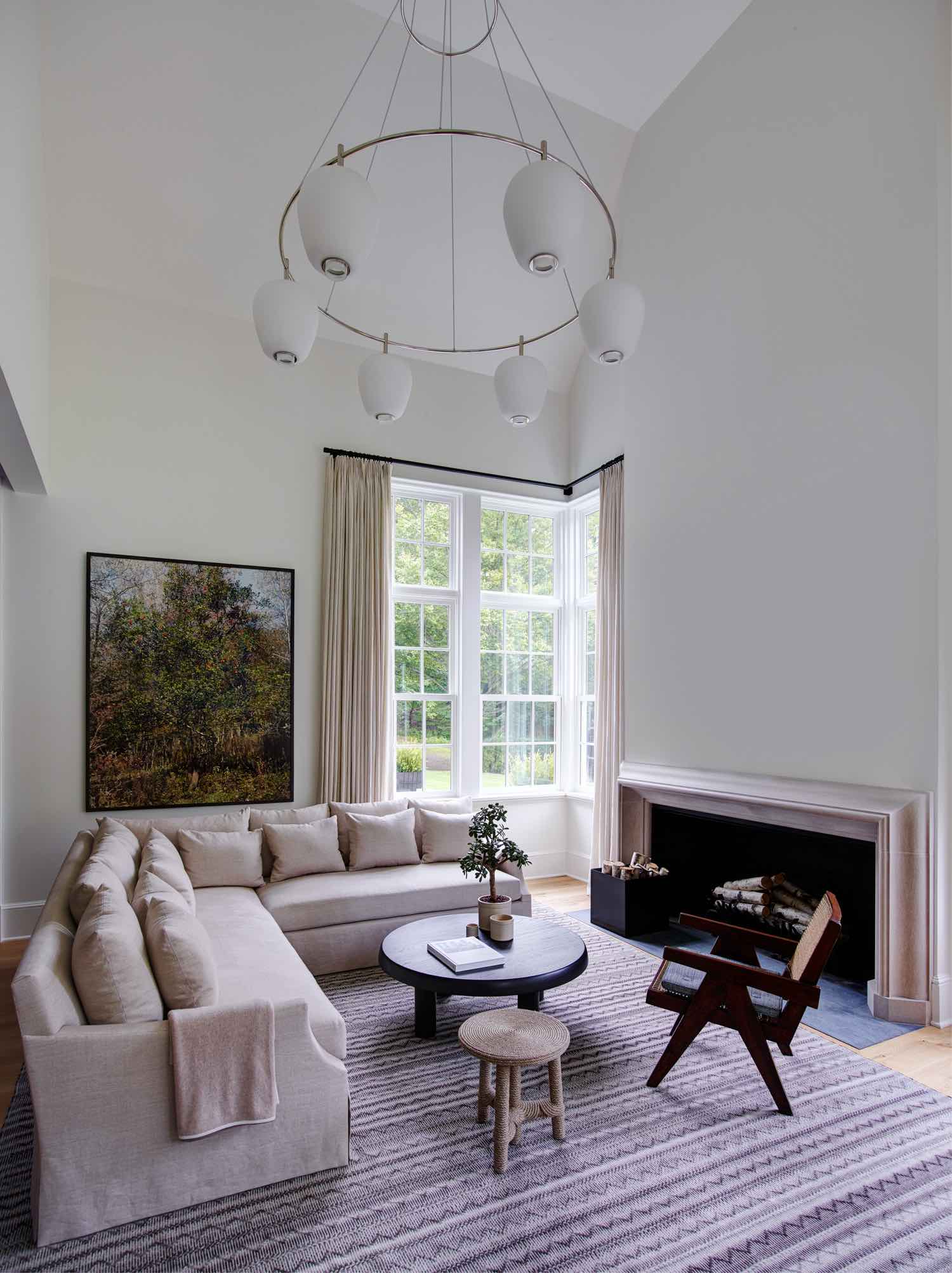 Designed by Carol Egan, the family rooms custom L shaped sofa is upholstered in a natural linen by Rogers & Goffigon.  The ebony wooden cocktail table designed by Charlotte Perriand and Afrido Rope stool by Chrstian Astuguevielle flank the sofa on a beautiful hand woven antural wool Sardinian rug by FJ Hakimian.  Opposite the sofa,  a lounge chair by Pierre Jeanneret in wood and caned finish.  A large vintage swedish ring light fixture fills the double height space.