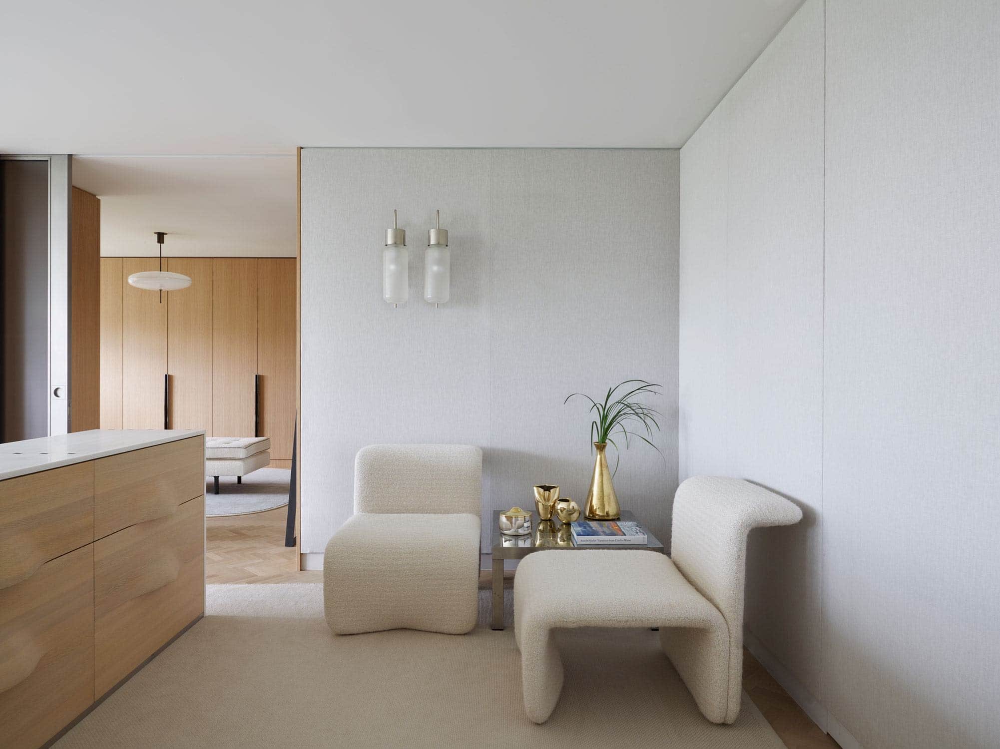 Designed by Carol Egan, this image shows the view as you enter the master bedroom in an apartment on Fifth Avenue in New York City which overlooks central Park.  A pair of Bidone wall lamps by Luigi Caccia Dominioni hang above a low steel triangle table by Francis See.  1968 chairs by Michel Boyerare placed side by side under the wall lights to expose the profile of the chair.  The walls are upholstered in a grey linen fabric and the area rug is a woven natural linen.