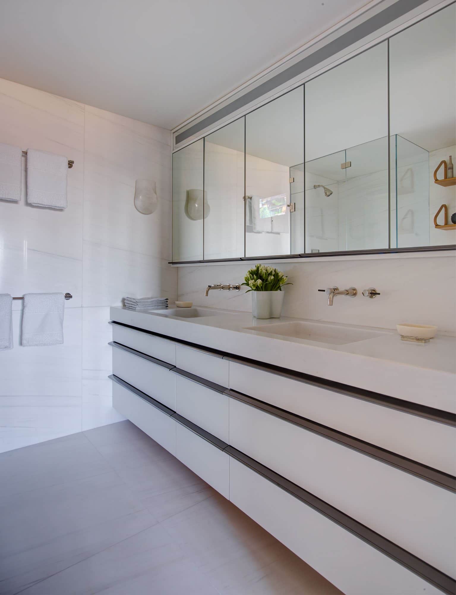 Designed by Carol Egan in a Fifth Avenue Apartment in New York, this image shows a Master Bathroom vanity fabricated in Dolomite Bianco honed marble stone with integrated sinks and backsplash.  A wall-to-wall mirror medicine cabinet hangs above the double vanity and the faucets are from the .25 waterworks series.