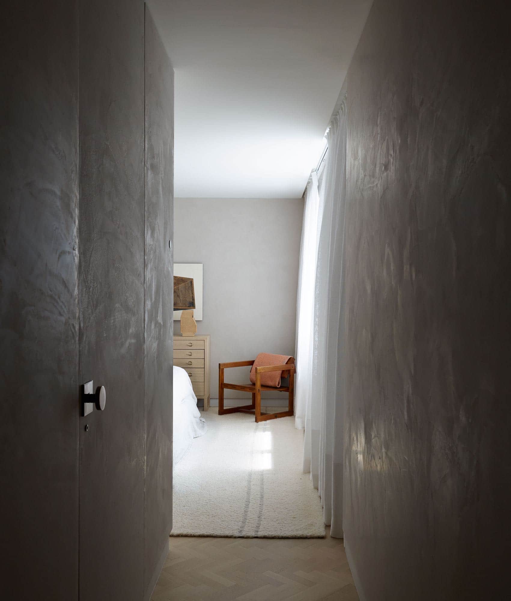 Designed by Carol Egan, this image is of a hallway leading into a guest bedroom.  The walls are plastered with a pale grey plaster and the floors are herringbone pattern in oak.  A "Found Box" artwork by Michael Zelehoski hangs on the far wall over a cabinet by Mogens Koch in Oak.  Swedish Architectural lounge chair by Edvin Helseth.