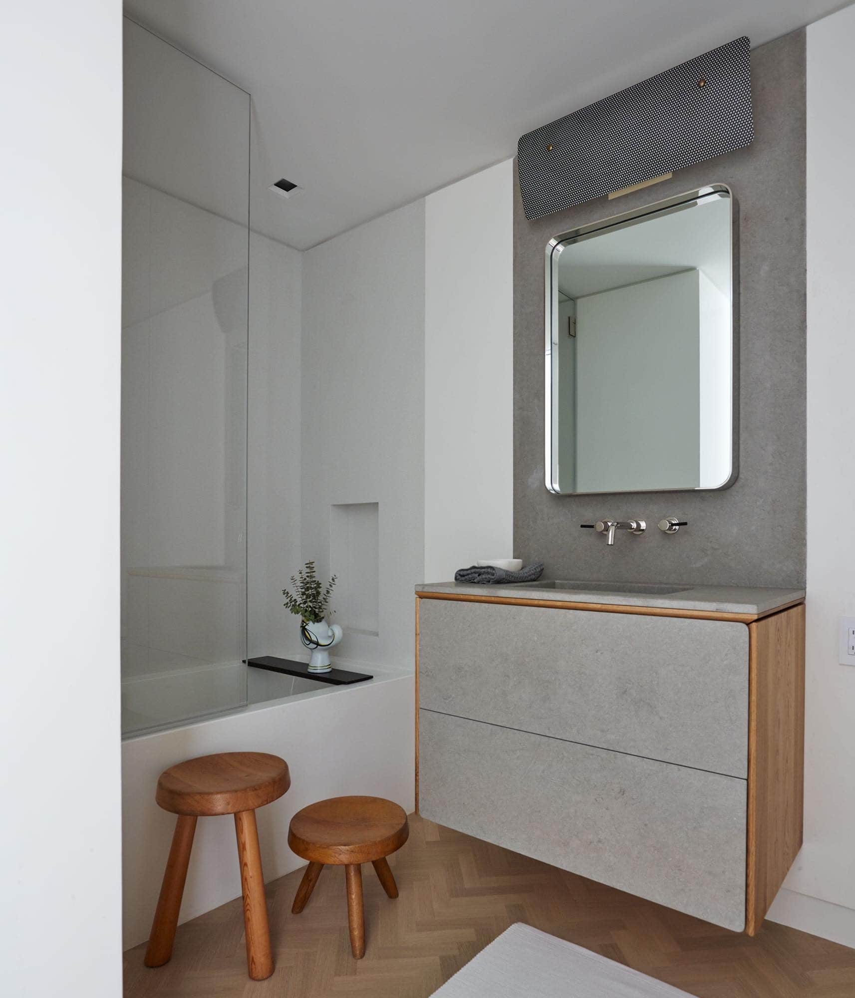 This photograph shows a guest bathroom designed by Carol Egan in a residence on Fifth Avenue in New York.  With a perforated rectangular vintage wall lamp by Pierre Guariche.   A square tailor washbasin integrated in a plana shelf and wall made of Sinai stone are inset into the bathroom plaster walls in a flush condition.  Stools are by Charlotte Perriand.