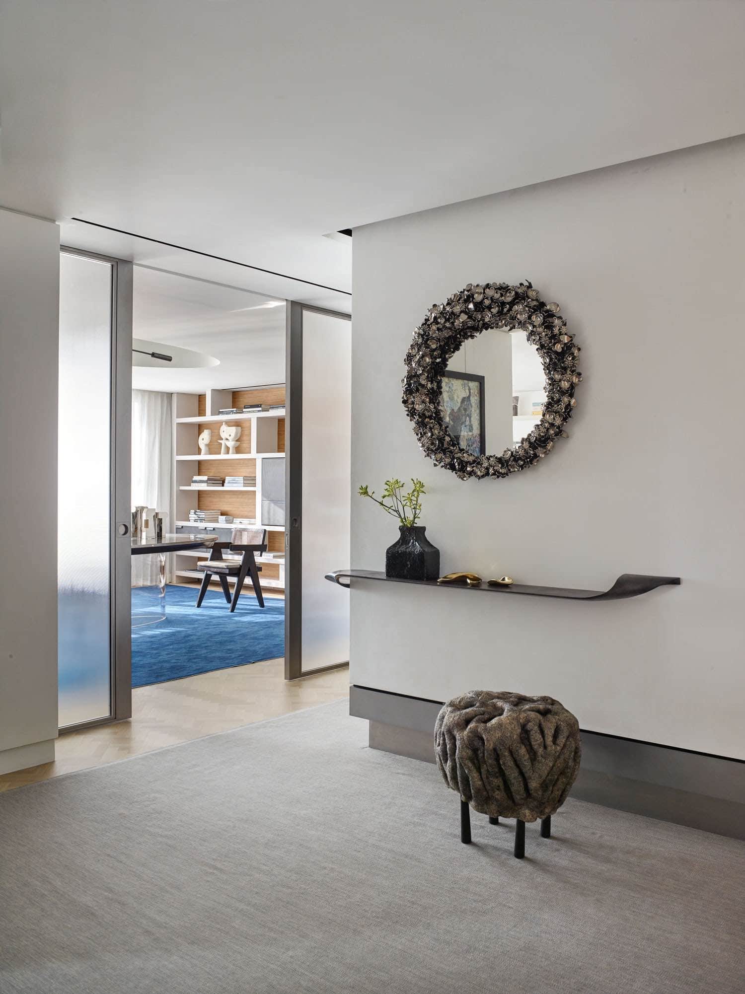 A view of the gallery in an apartment on Fifth Avenue overlooking Central Park in New York City designed by Carol Egan showcasing a "Mirror Mirror" by Barnaby Barford in ceramic above a custom wall hung twist shelf - leather wrapped by Studio Carol Egan and a Shastool footstool by Ayala Serfaty.  Floor covering by FJ Haikimian.