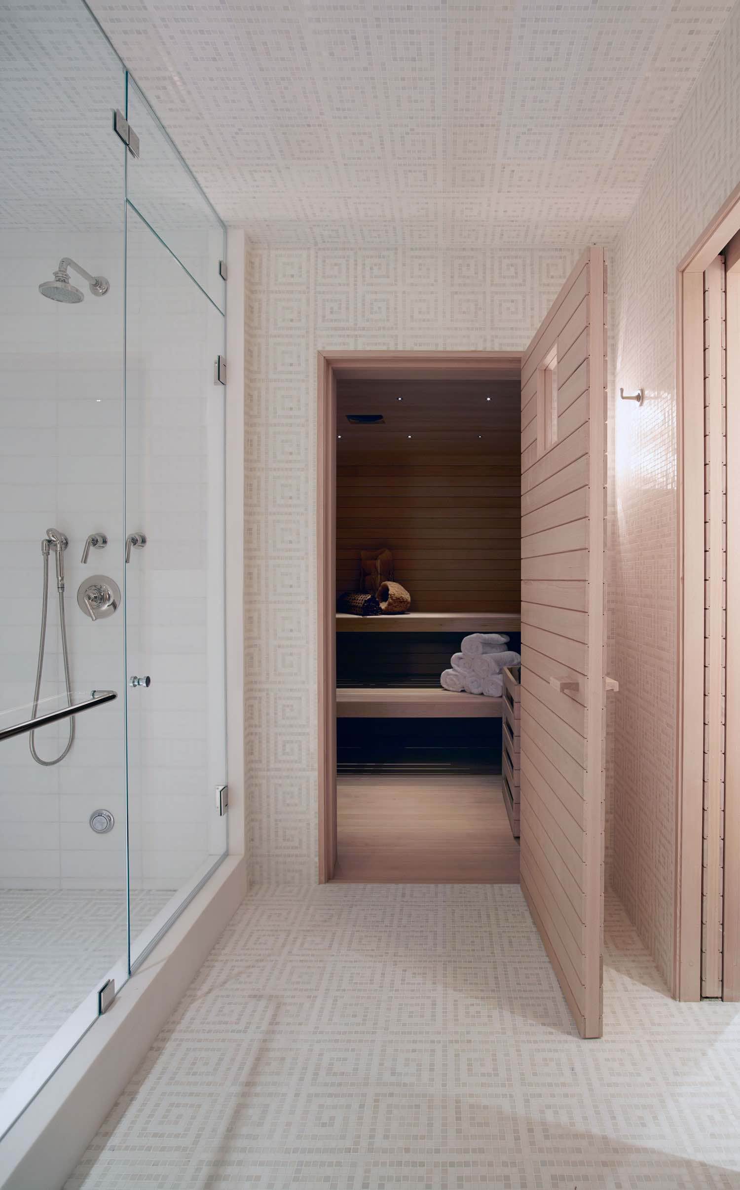 This image shows a sauna room designed by Carol Egan in mosaic Spartan Maze Field tile by Urban Archaeology.  The Sauna door is opened to the adjacent marble bathroom with plumbing fixtures from the Henry Collection supplied by Waterworks.