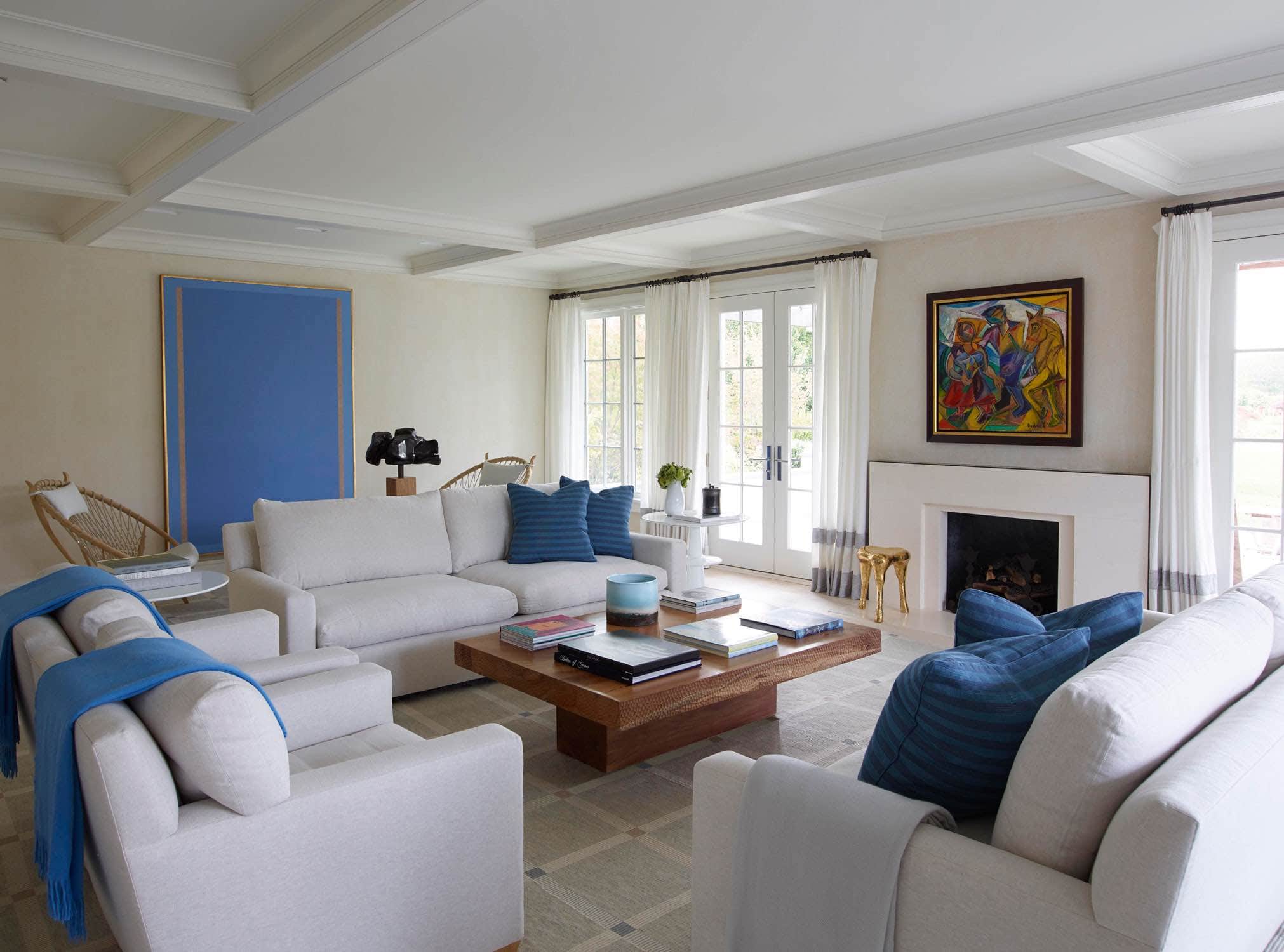 Designed by Carol Egan, this image shows a view of the living room with JMF style sofas in linen flanking a pedestal wood coffee table by tucker Robbins.  The oil on canvas painting over the fireplace is titled "Peasants and Horse" by David Burliuk Haziea.  Sculpture by Zigor can been seen on a console table behind the sofa and the solar occasional table by Holly Hunt bookend each sofa.  By the fireside is a Hex stool by The Haas Brothers.  Window Treatment in custom woven silk Chenille & Strie banding by Sam Kasten.  Solid cashmere throws in Azure by Holland & Sherry.  Hand woven area rug in large grid pattern by Elizabeth Eakins.