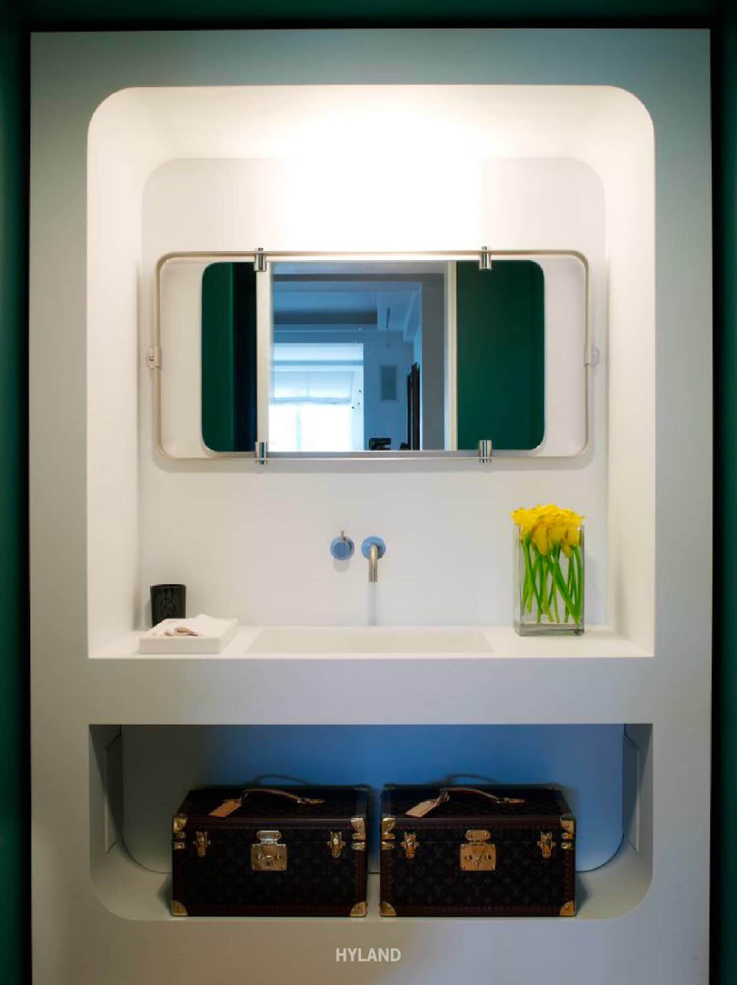 The powder room is made of white Corian framework enclosing the sink and shelves with "Modernist" mirror from John Salibello Antiques and train case by Louis Vuitton.